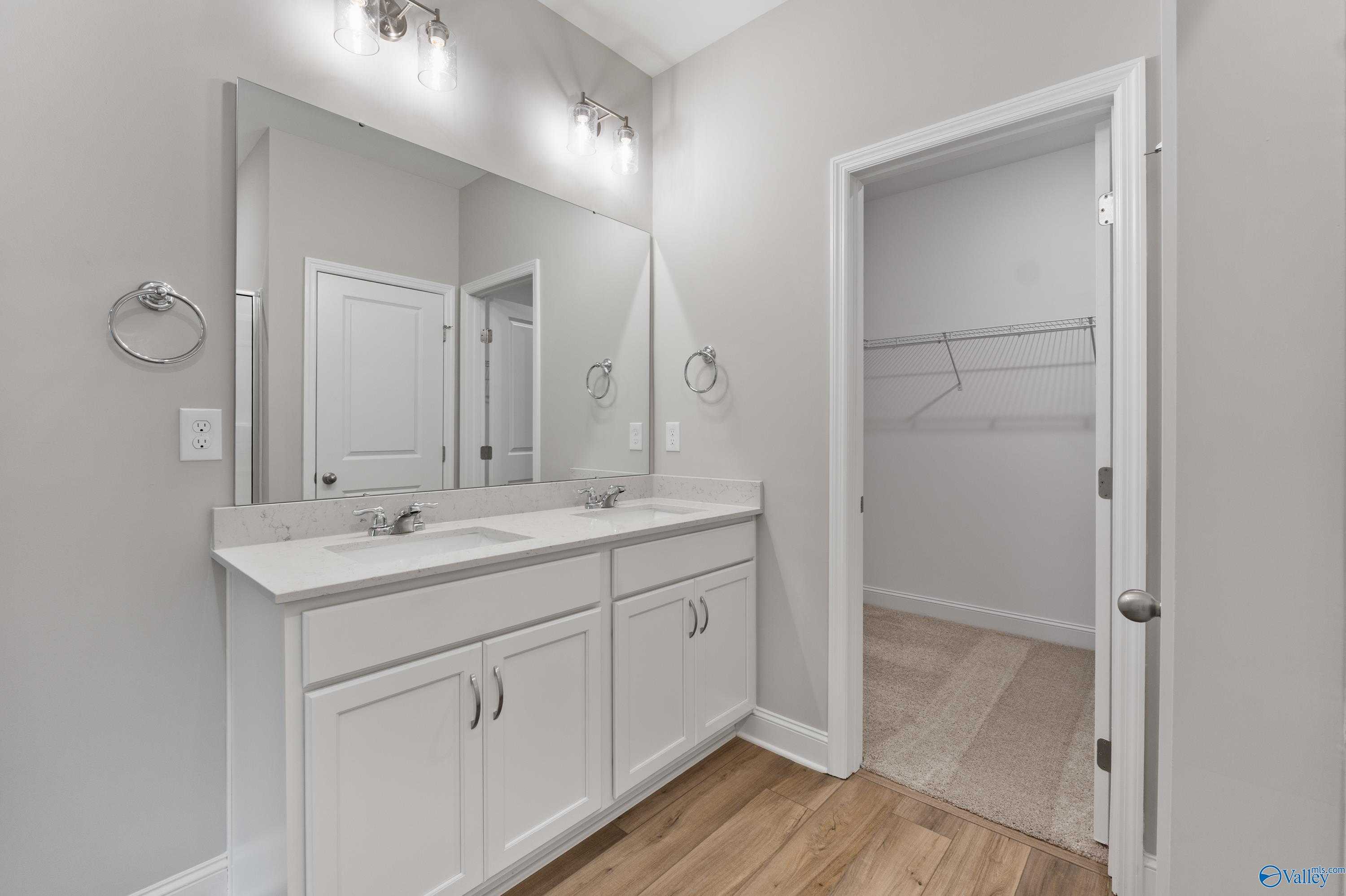 Modern master bathroom featuring double vanity sinks, mirrors, and adjacent walk-in closet in Davidson Homes The Franklin, Huntsville, Alabama