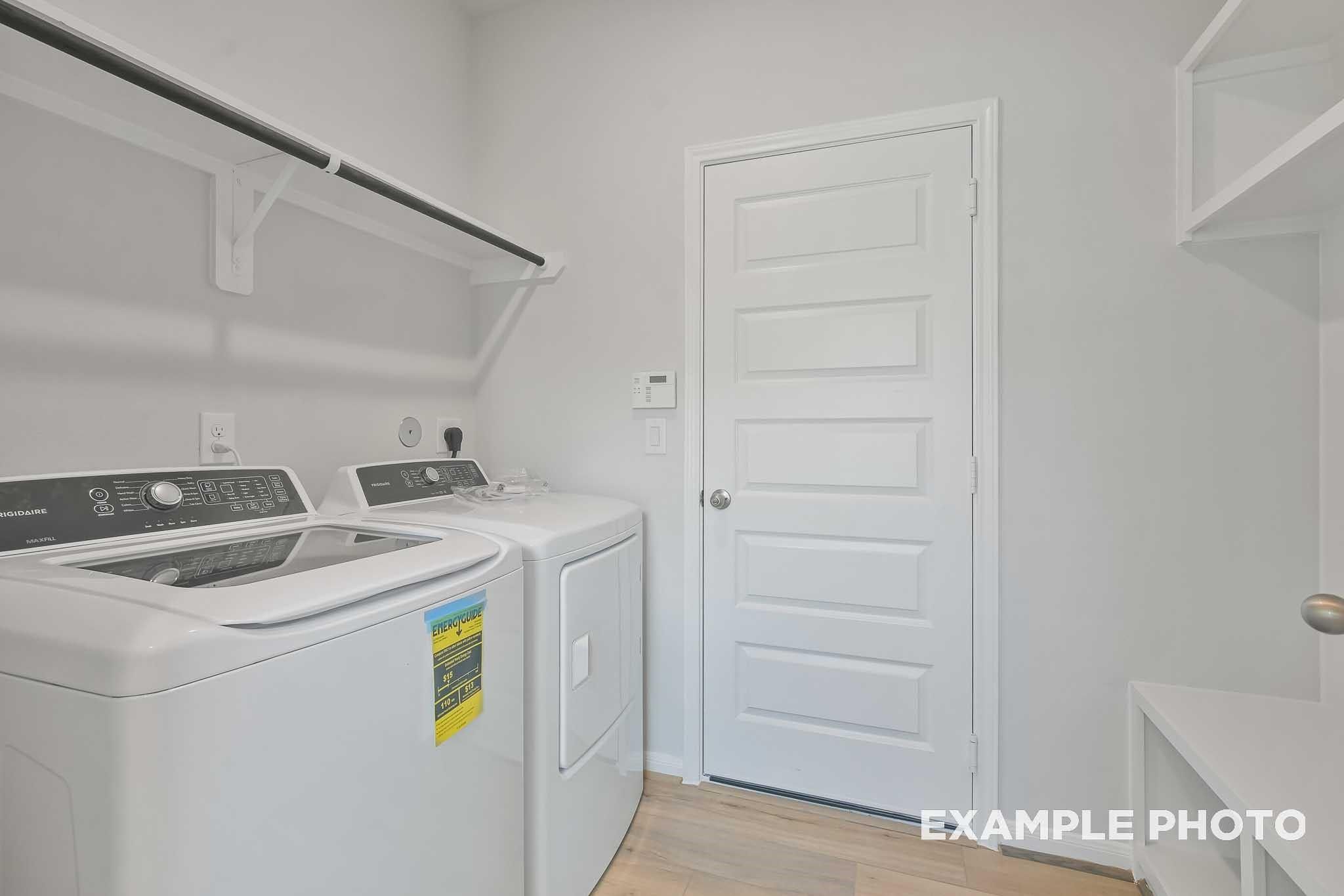Modern laundry room with white washer-dryer set, built-in shelves, and adjacent door in Davidson Homes The Frio F, Conroe Texas