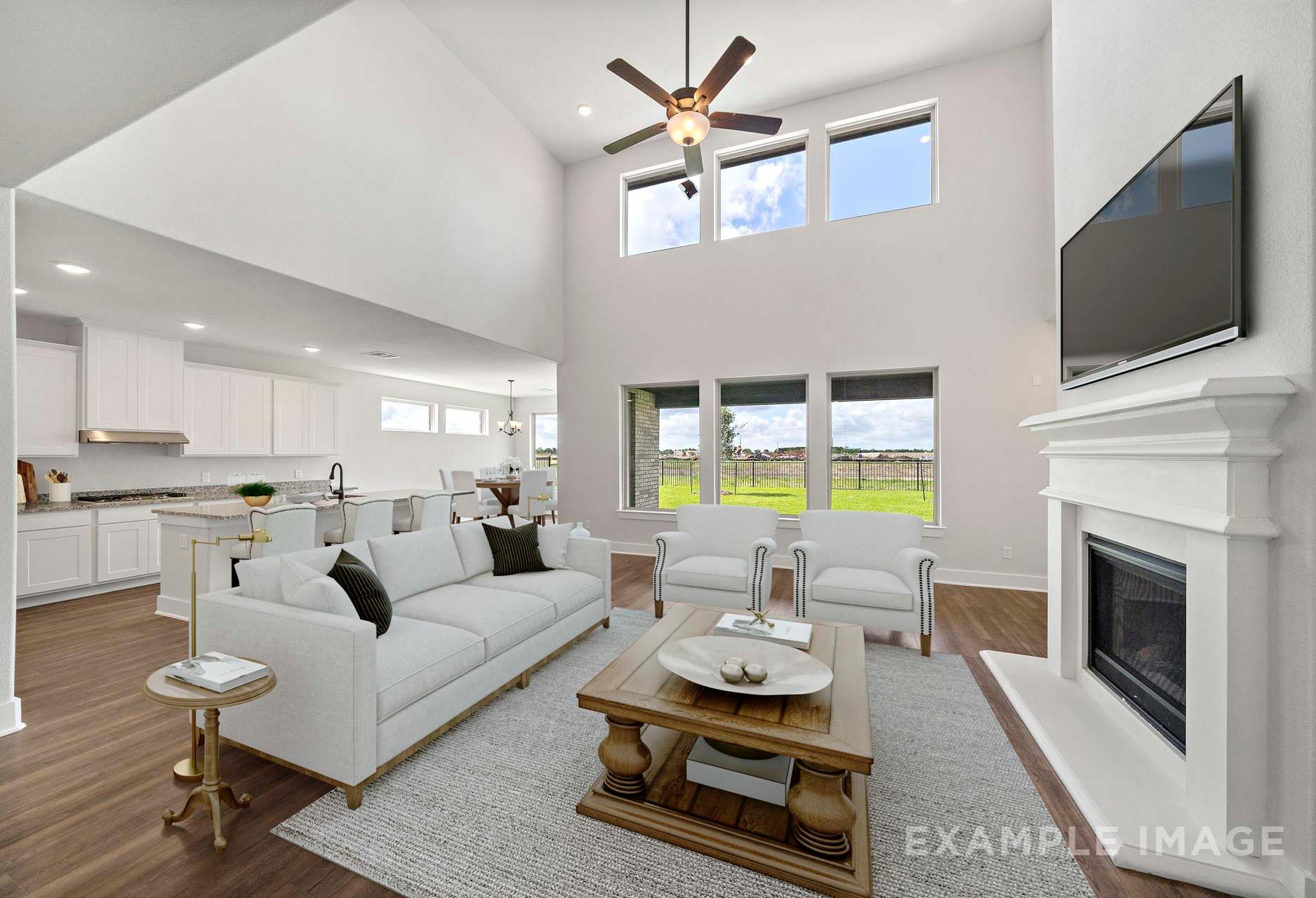 Spacious open-concept great room in The Victoria A with vaulted ceilings, white fireplace, modern sofa, and kitchen island