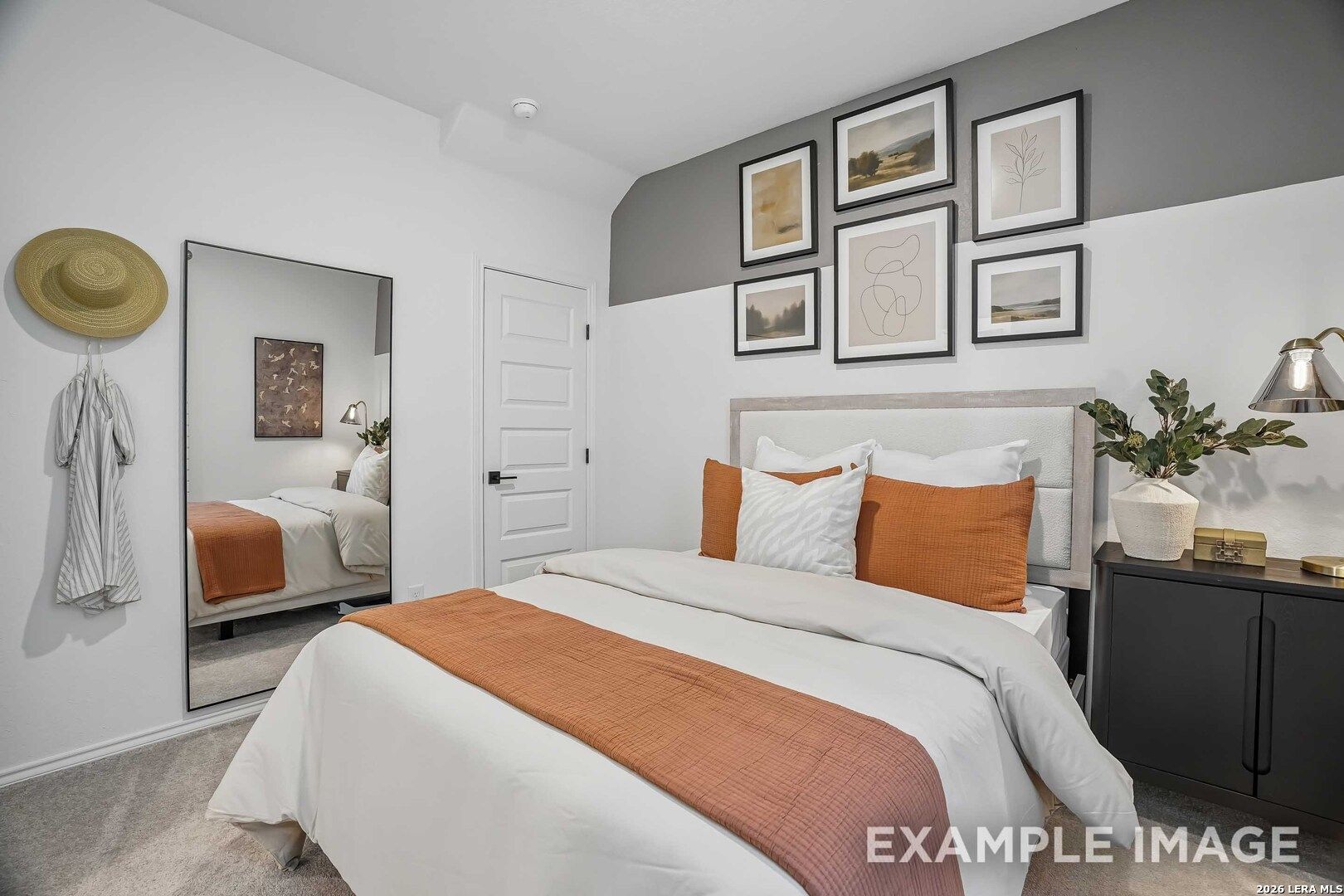 Cozy bedroom with orange accent bedding, gallery wall, and full-length mirror in Davidson Homes Pinecrest E, Converse, Texas