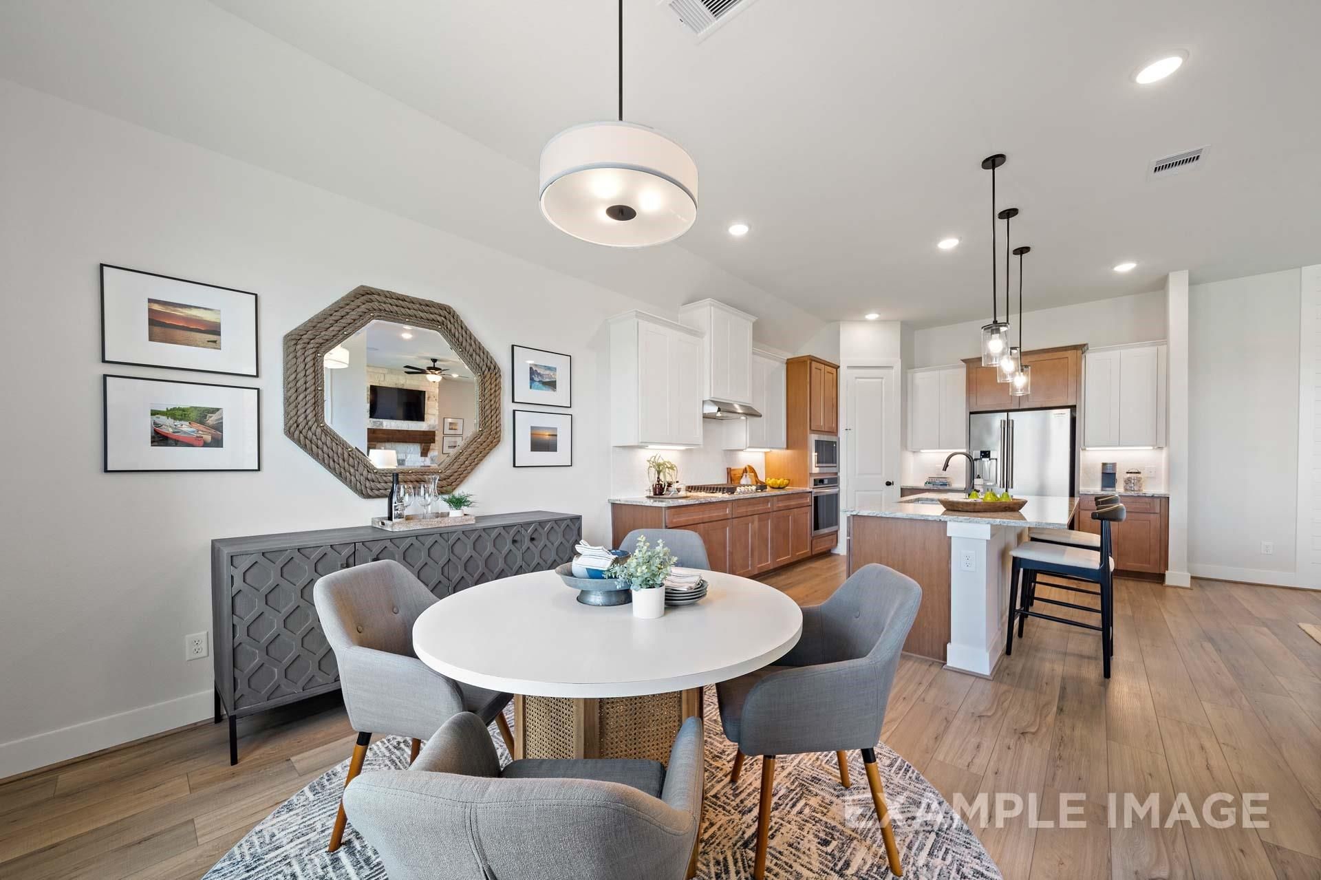 Modern dining area with round white table, gray chairs, and large mirror beside open kitchen in Davidson Homes The Edward A, Texas City