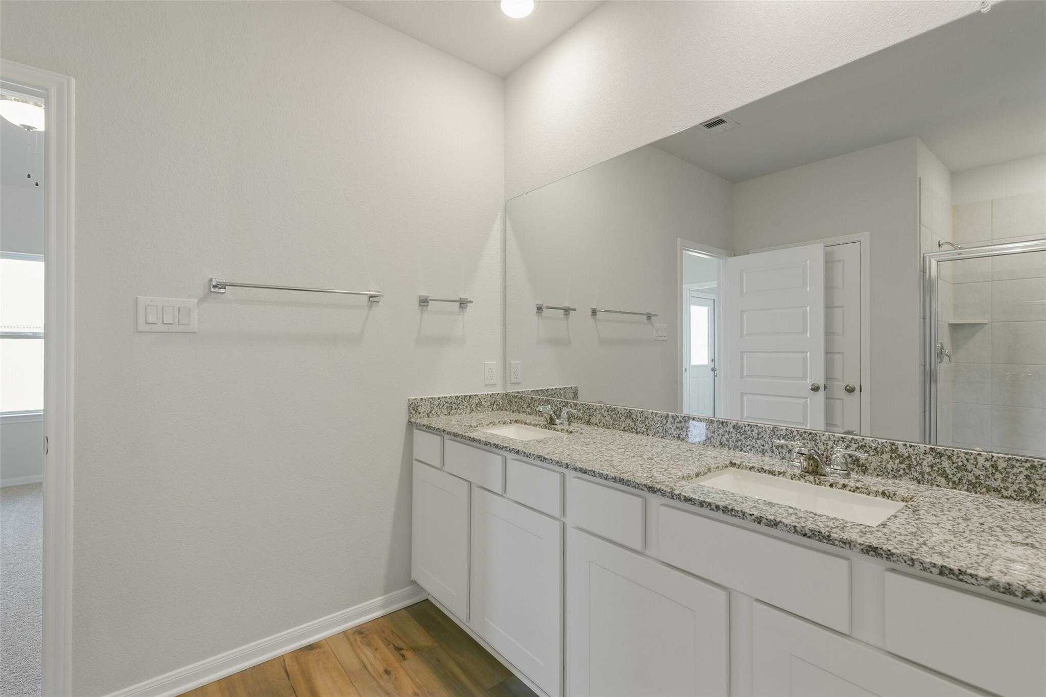 Modern master bathroom with double granite vanity, white cabinets, large mirror, and walk-in shower in The Laguna B, Dayton, Texas