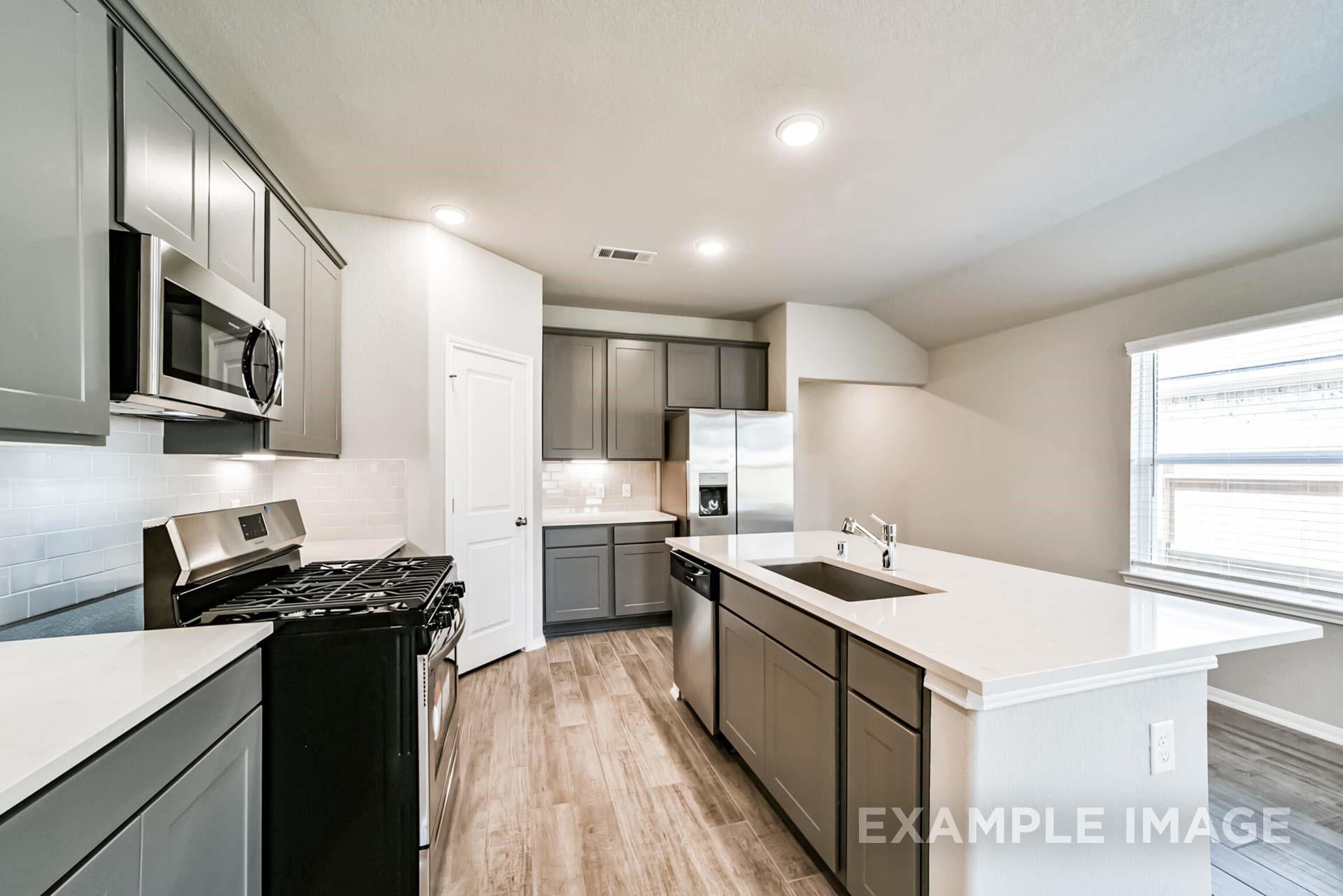 Modern kitchen with grey cabinets, quartz island, and stainless appliances in The Riviera A home at Emberly in Beasley, TX.