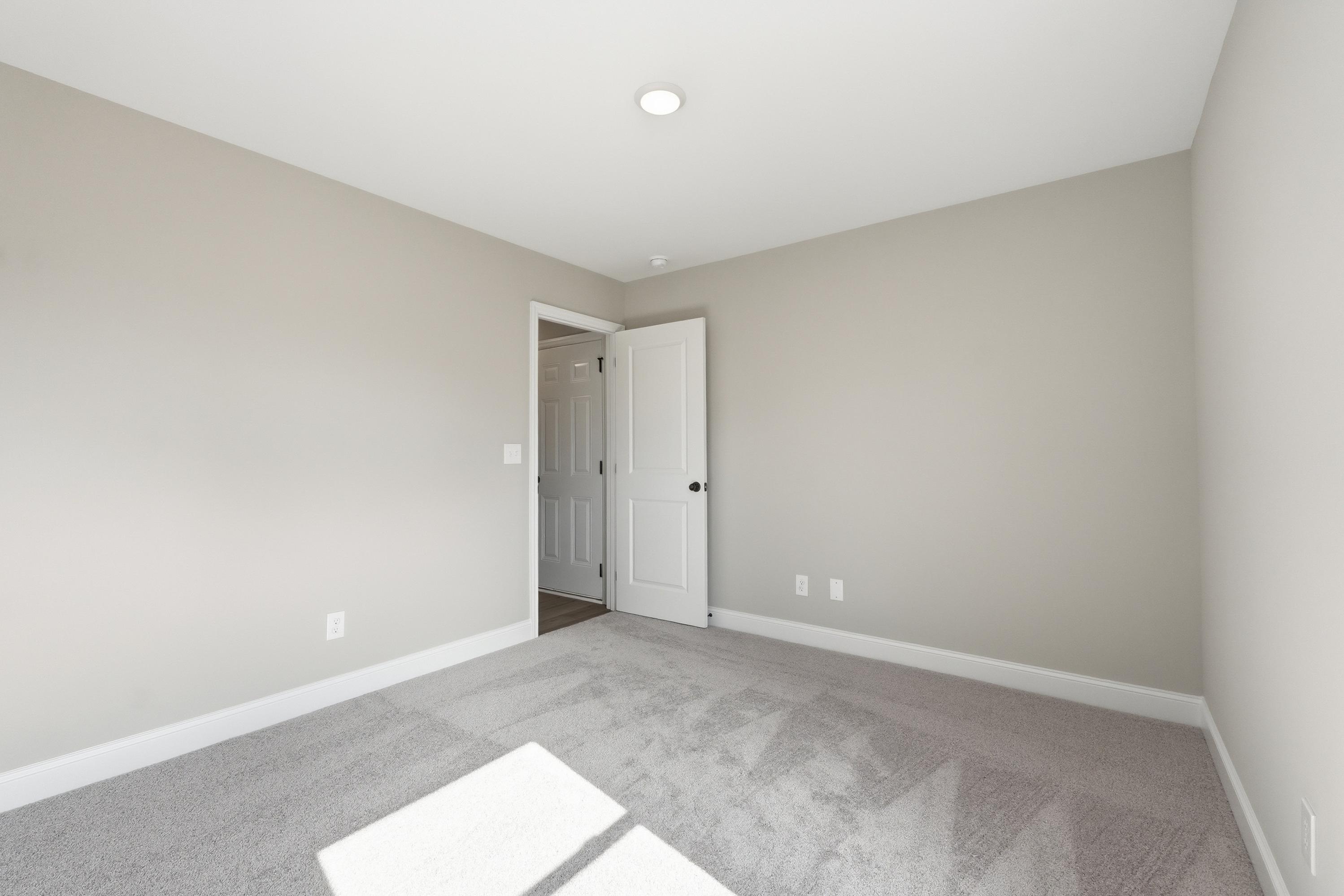 Spacious secondary bedroom in The Daphne V with neutral beige walls, gray carpet flooring, and open white door