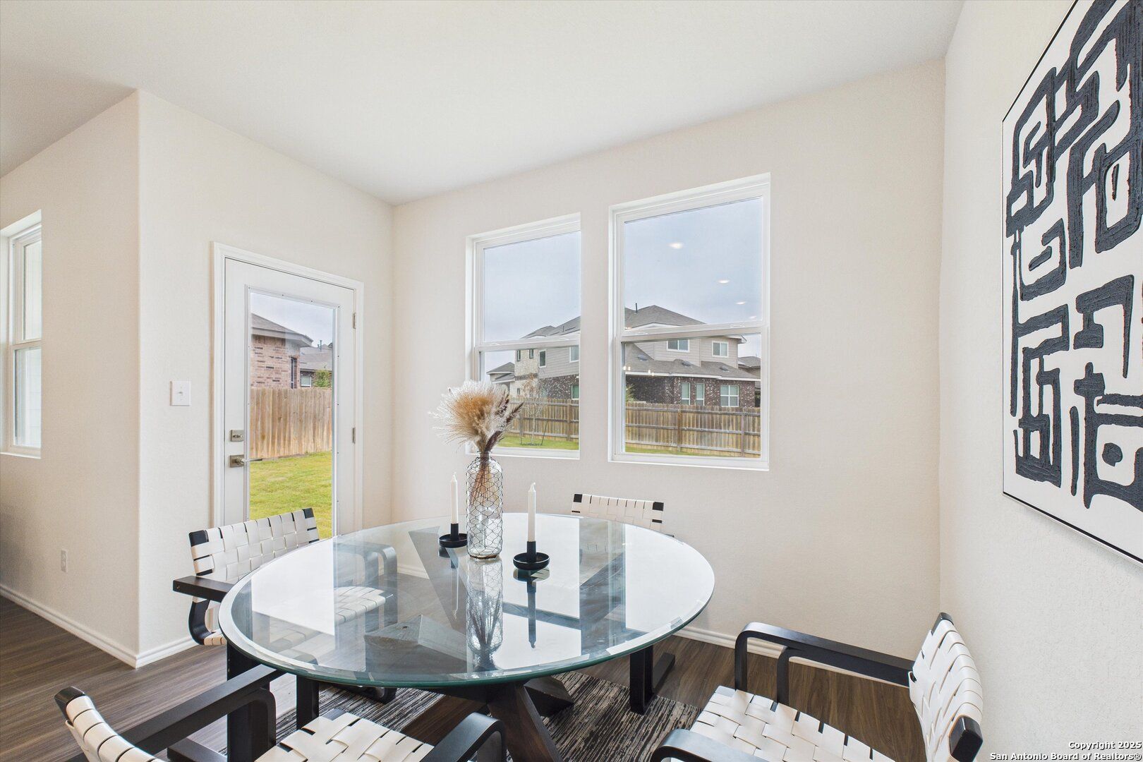Modern dining room with round glass table, white chairs, and backyard view in Davidson Homes The Asheville K, Bricewood, San Antonio