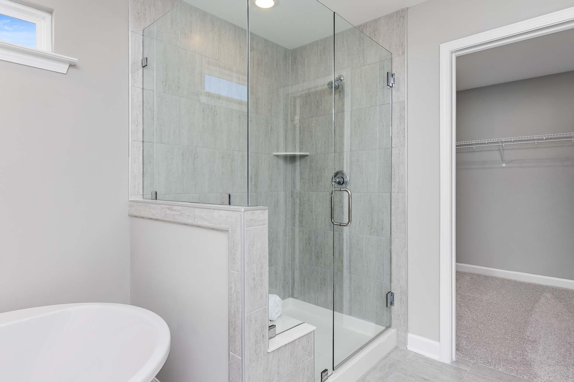 Modern primary bathroom with frameless glass shower, gray subway tile, and walk-in closet at Highland Forest in Fuquay-Varina NC