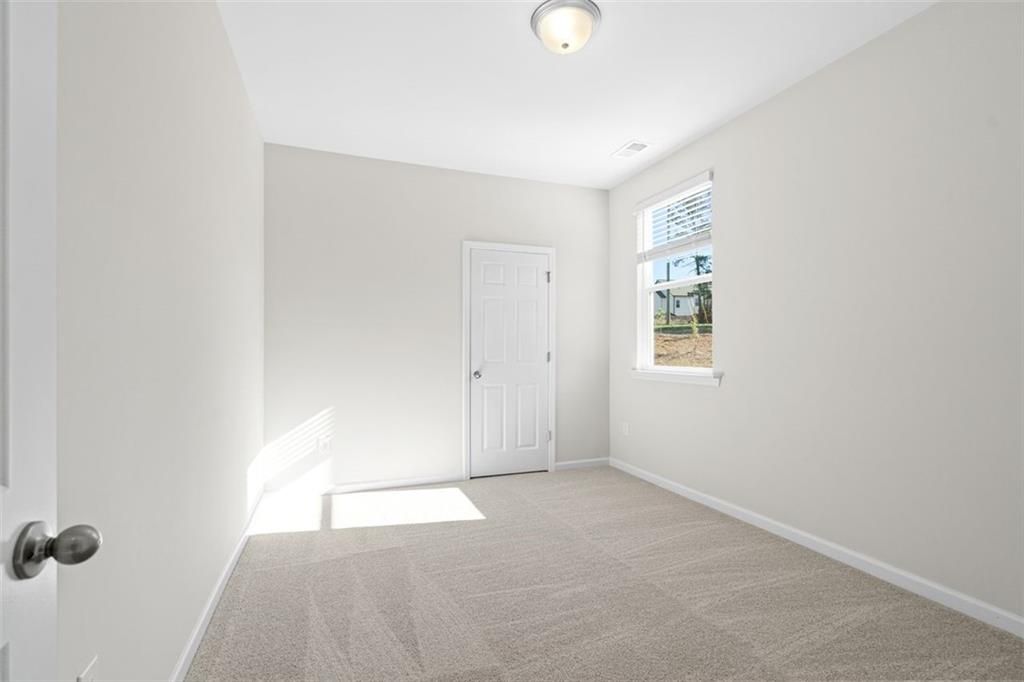Bright empty bedroom with neutral walls, carpet flooring, and large window in Davidson Homes The Glenwood C, Wehunt Meadows, Hoschton