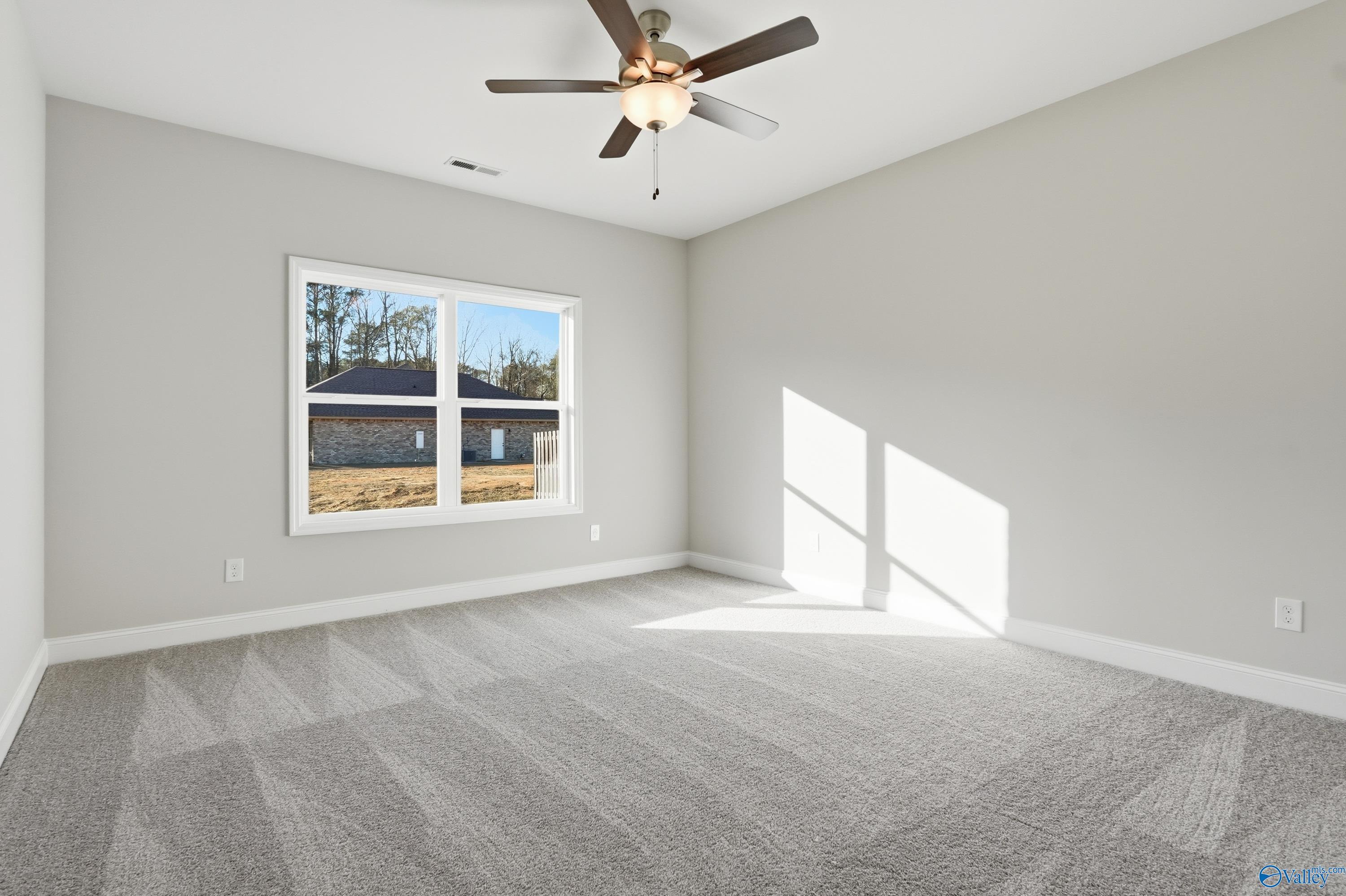 Bright empty bedroom with ceiling fan, large window overlooking woods, and gray carpet in Davidson Homes The Daphne C, Arab, Alabama