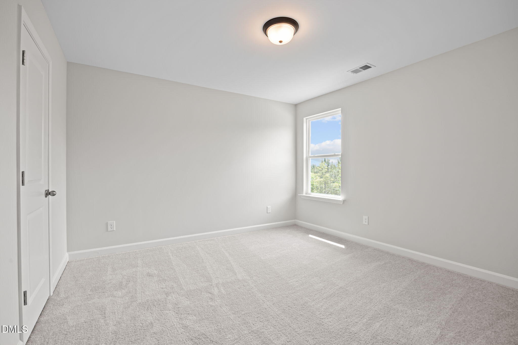 Bright empty bedroom with neutral gray walls, plush carpet, ceiling light, and window view of trees in Davidson Homes The Willow D, Wendell, NC