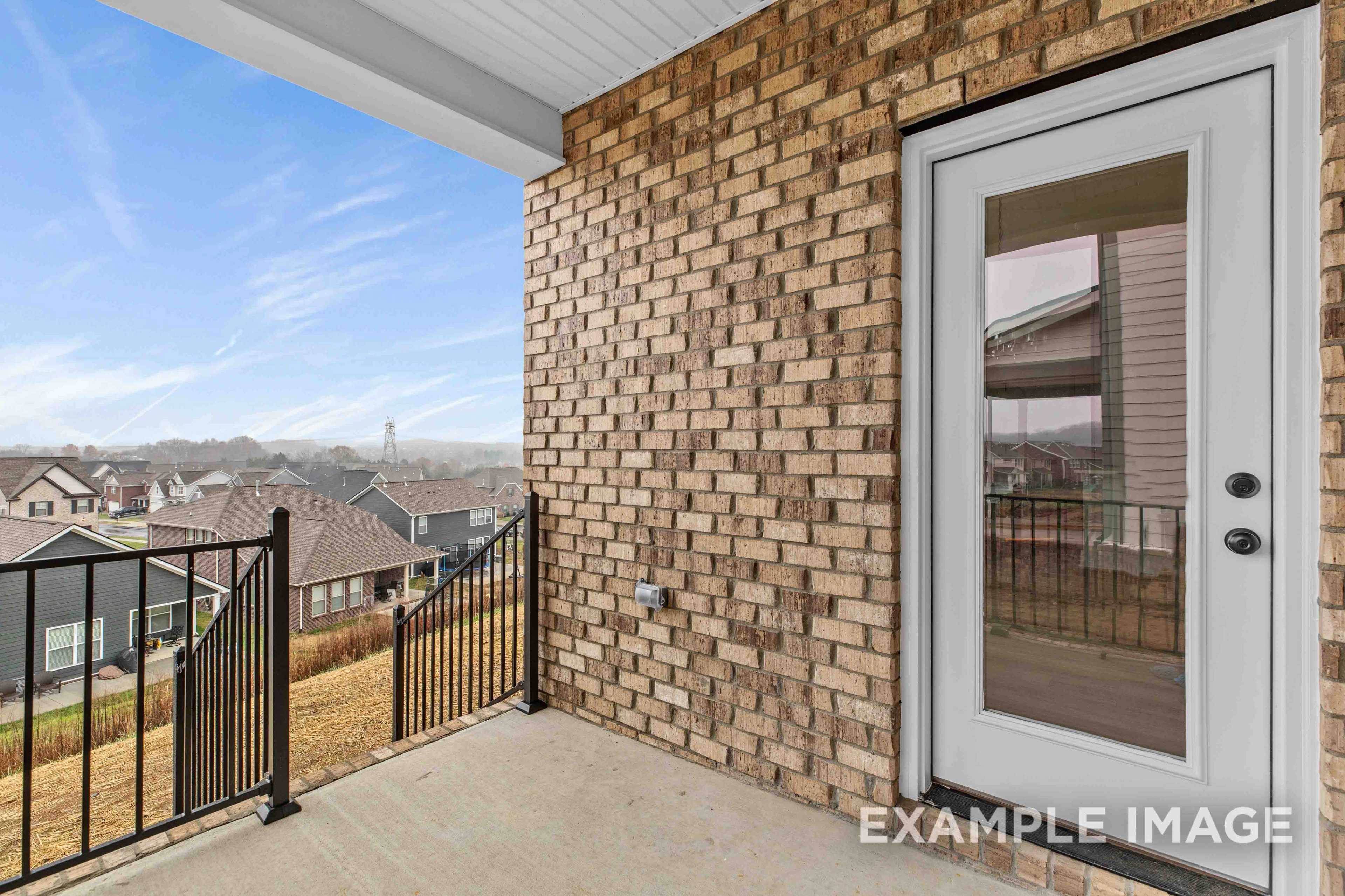 Upper balcony of the Charleston C home with brick exterior, glass doors, black railing, and scenic Mt. Juliet neighborhood view