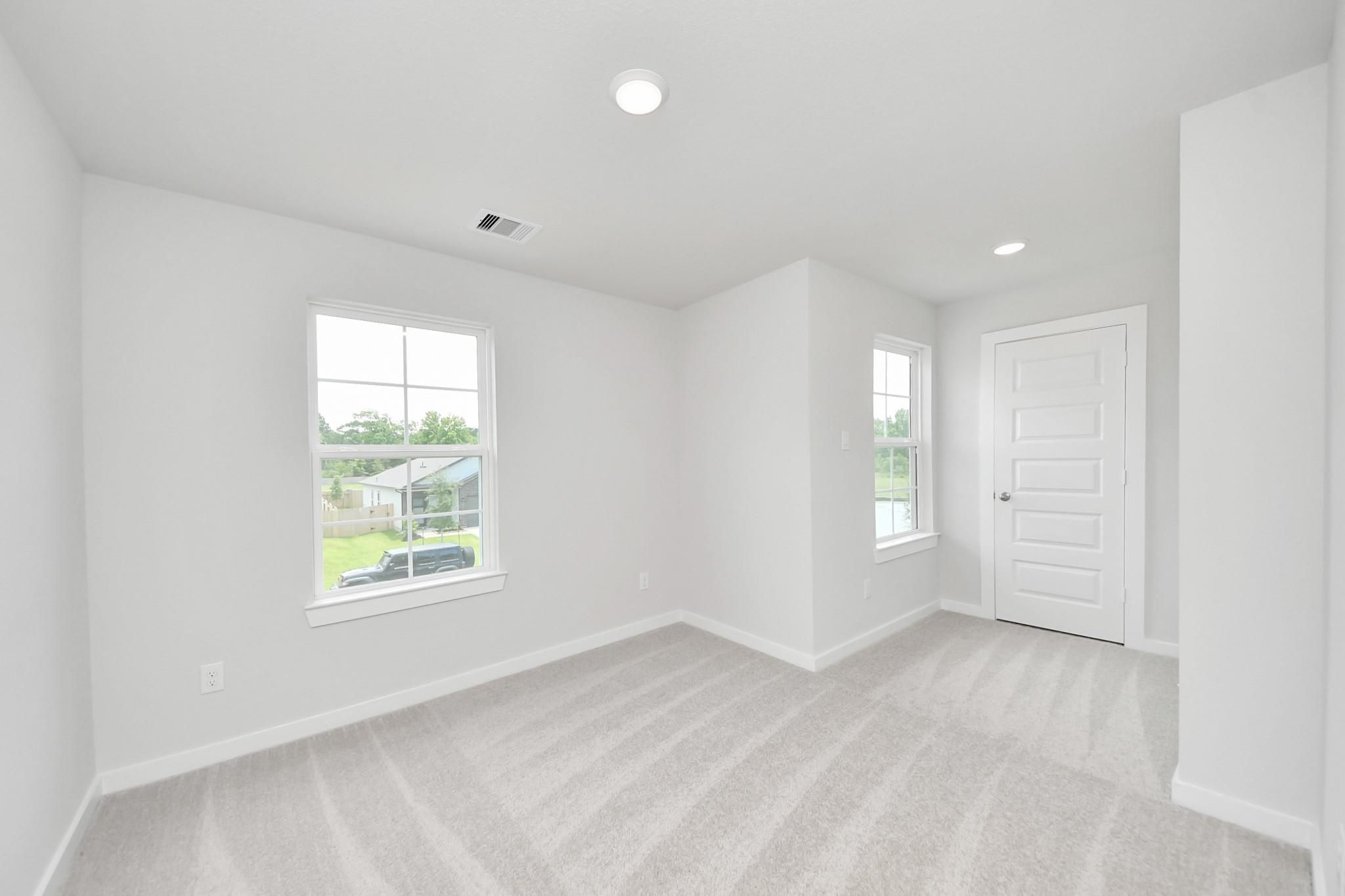Bright, carpeted bedroom with large windows in The Blanco E floor plan at Caney Creek Place, Conroe, Texas.