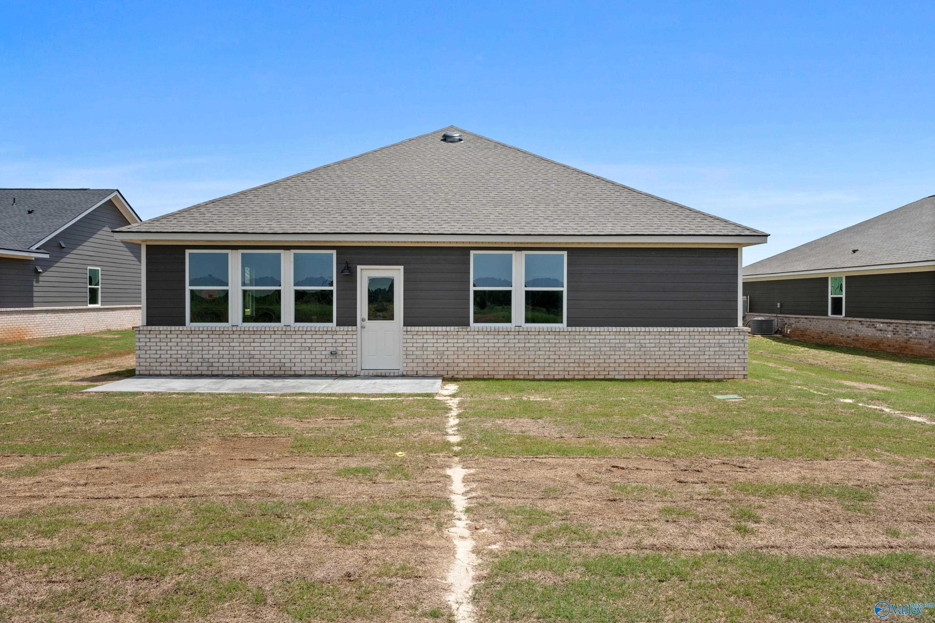 Rear view of single-story 4-bedroom Davidson Homes Orion with gray siding, large windows, and brick base in Anderson Farm, Athens, Alabama