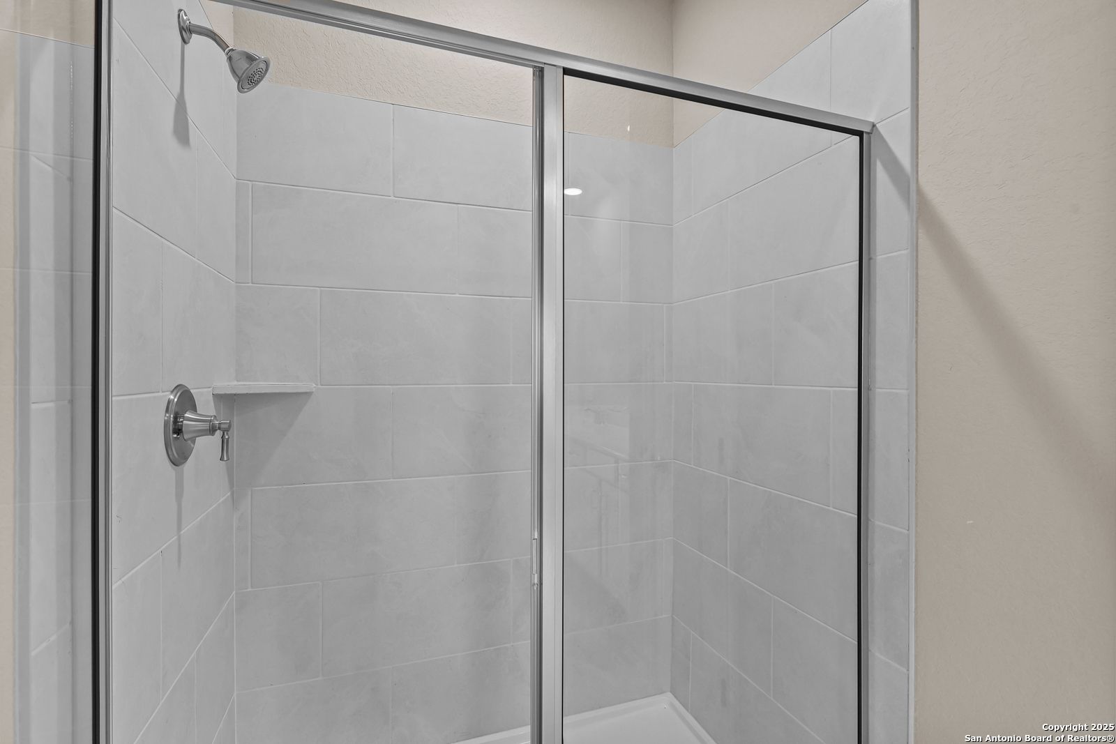 Modern frameless glass shower with white subway tiles, chrome fixtures, and built-in shelf in Davidson Homes The Douglas G, San Antonio