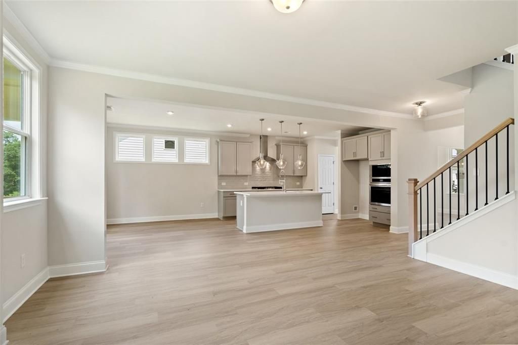 Open-concept kitchen with white island, stainless appliances, pendant lights, hardwood floors, and staircase in Davidson Homes The Willow D at Wehunt Meadows, Hoschton