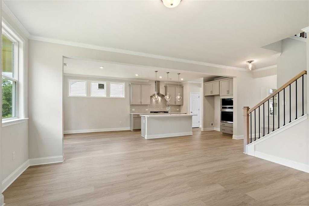 Open-concept kitchen with white island, stainless appliances, pendant lights, hardwood floors, and staircase in Davidson Homes The Willow D at Wehunt Meadows, Hoschton