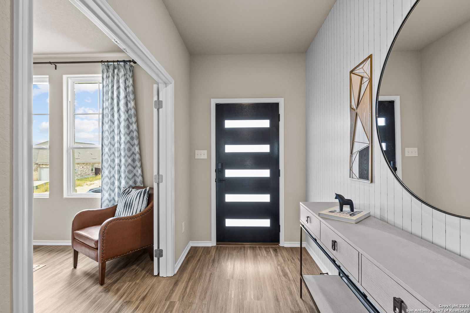Elegant entry foyer with black front door, gold-framed mirror, console table, leather armchair in Davidson Homes The Douglas F, Bricewood San Antonio