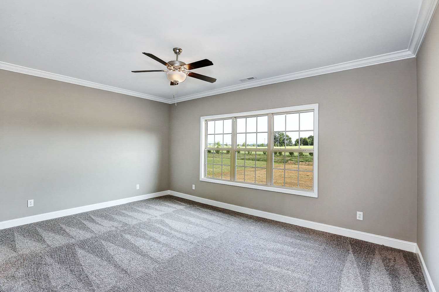 Spacious master bedroom in The Montgomery Davidson Homes design with gray walls, ceiling fan, and large windows overlooking fields