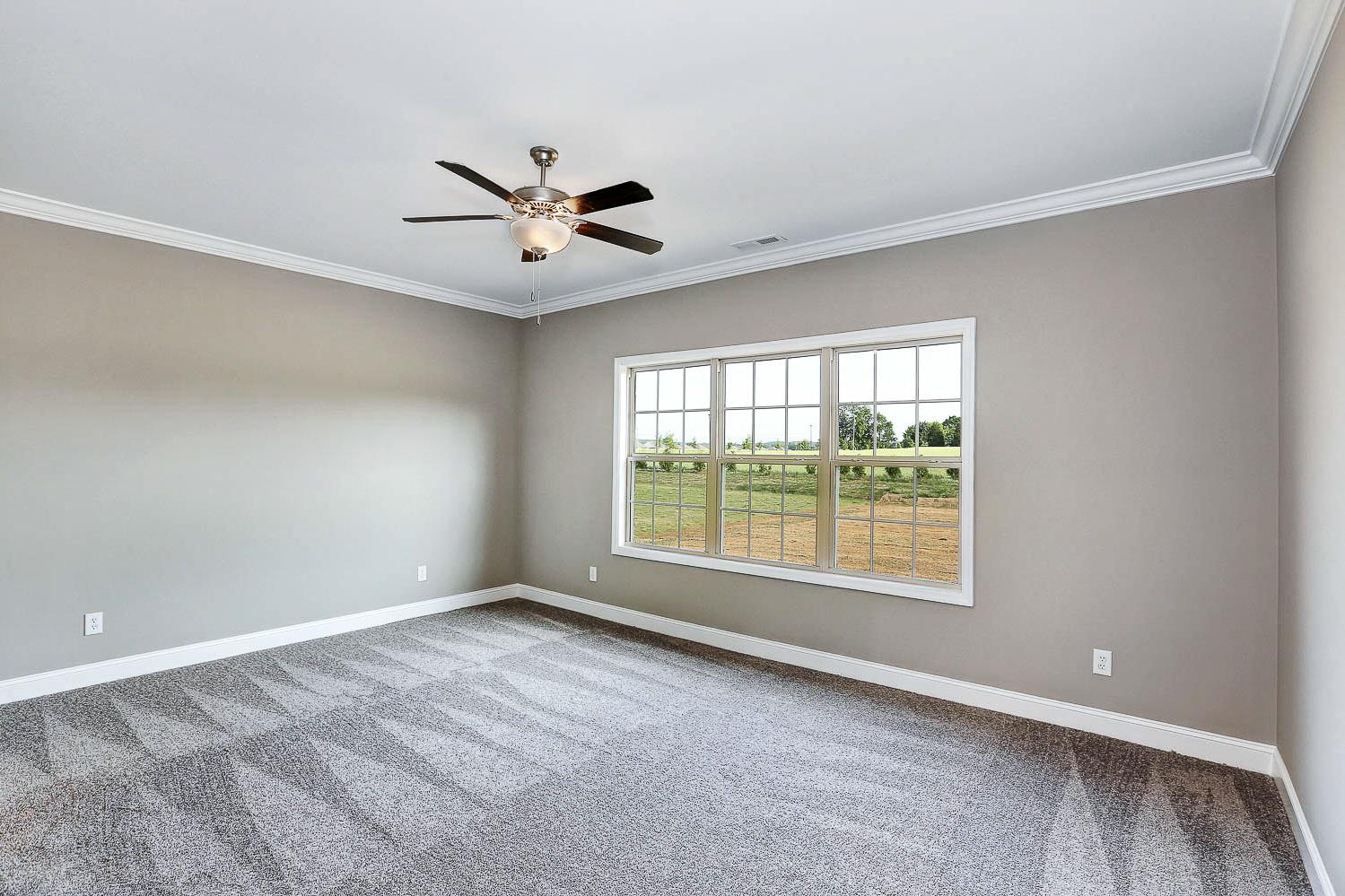 Spacious master bedroom in The Montgomery Davidson Homes design with gray walls, ceiling fan, and large windows overlooking fields