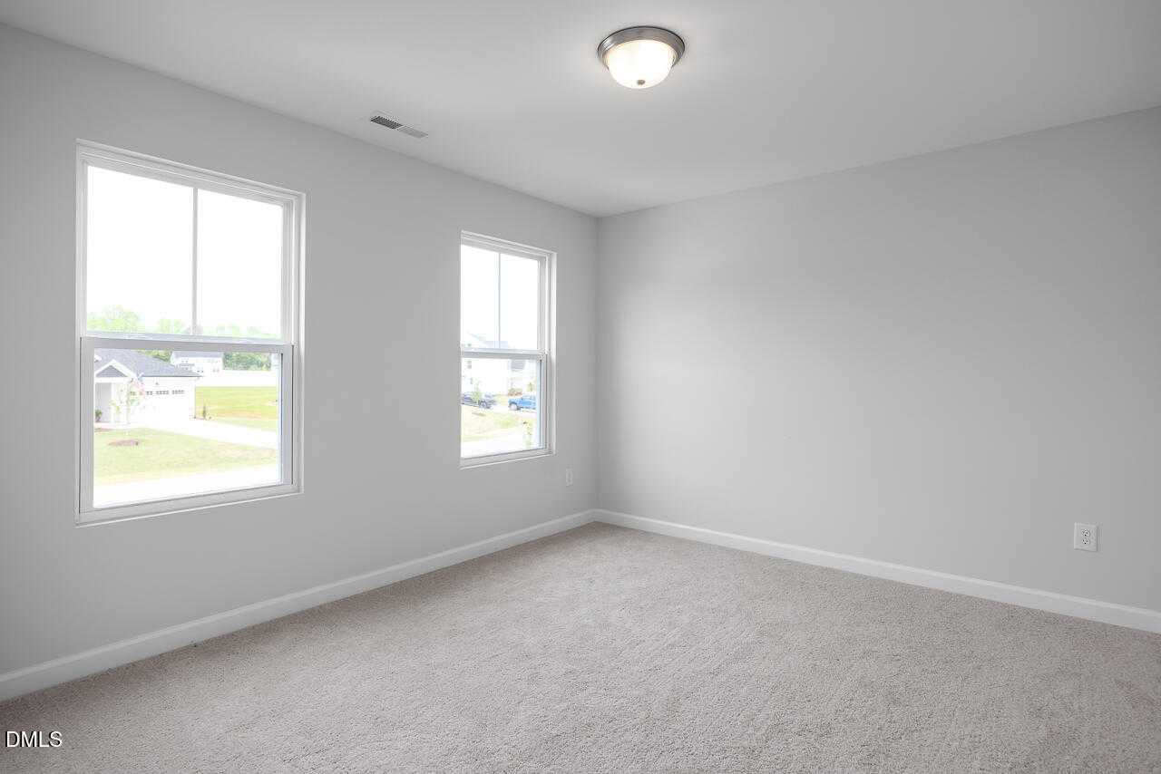 Spacious empty bedroom with gray walls, large double windows, neutral carpet in 5-bed Davidson Homes The Hickory II B, Zebulon, NC