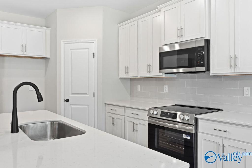 Modern white kitchen with shaker cabinets, stainless steel appliances, quartz island, and subway tile backsplash in The Montgomery B, Hartselle, AL