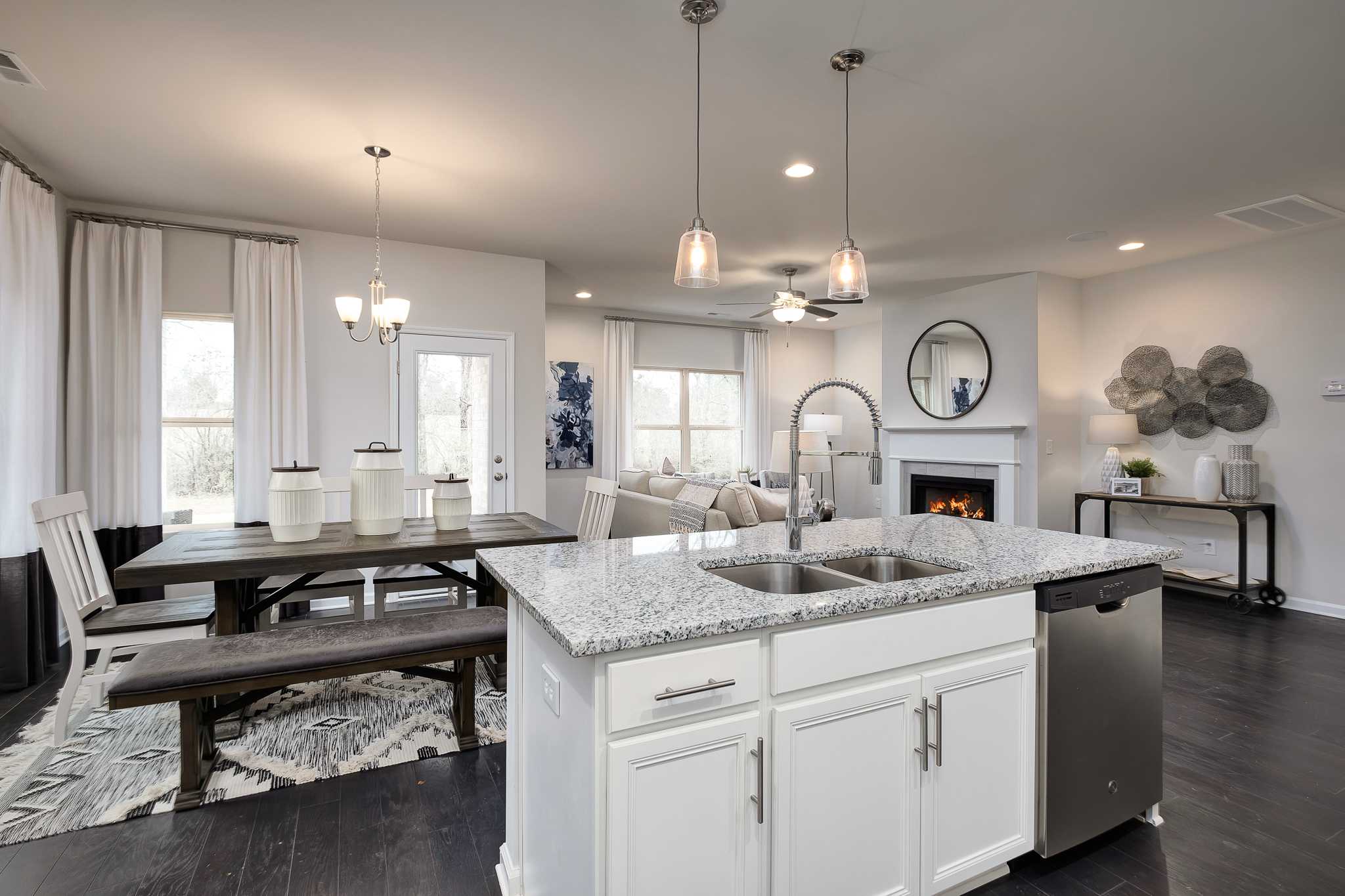 Open-concept kitchen and living room at The Reserve at Overton in Hampton Cove AL featuring white cabinets, granite island, gas fireplace, and hardwood floors