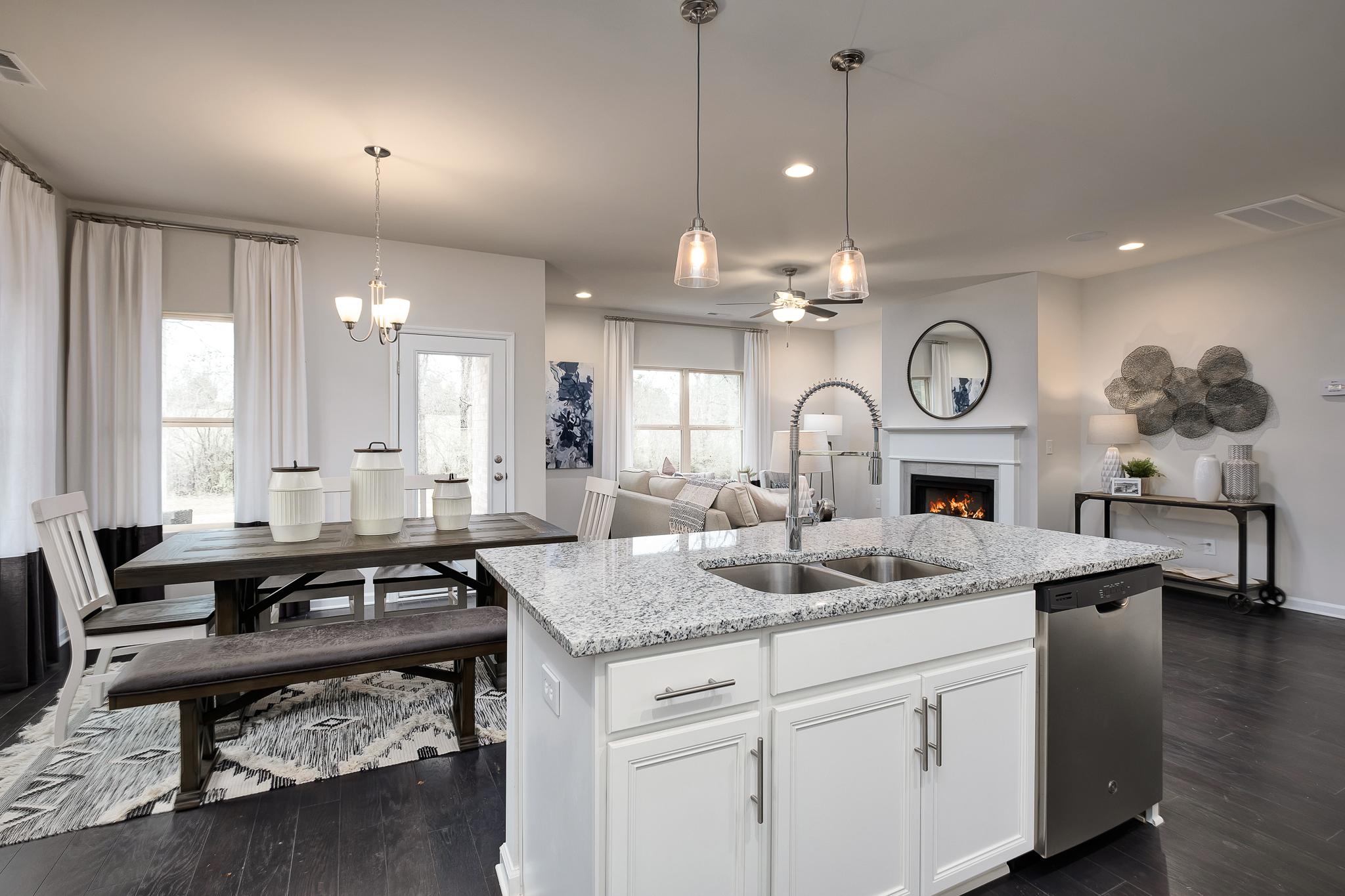 Open-concept kitchen and living room at The Reserve at Overton in Hampton Cove AL featuring white cabinets, granite island, gas fireplace, and hardwood floors