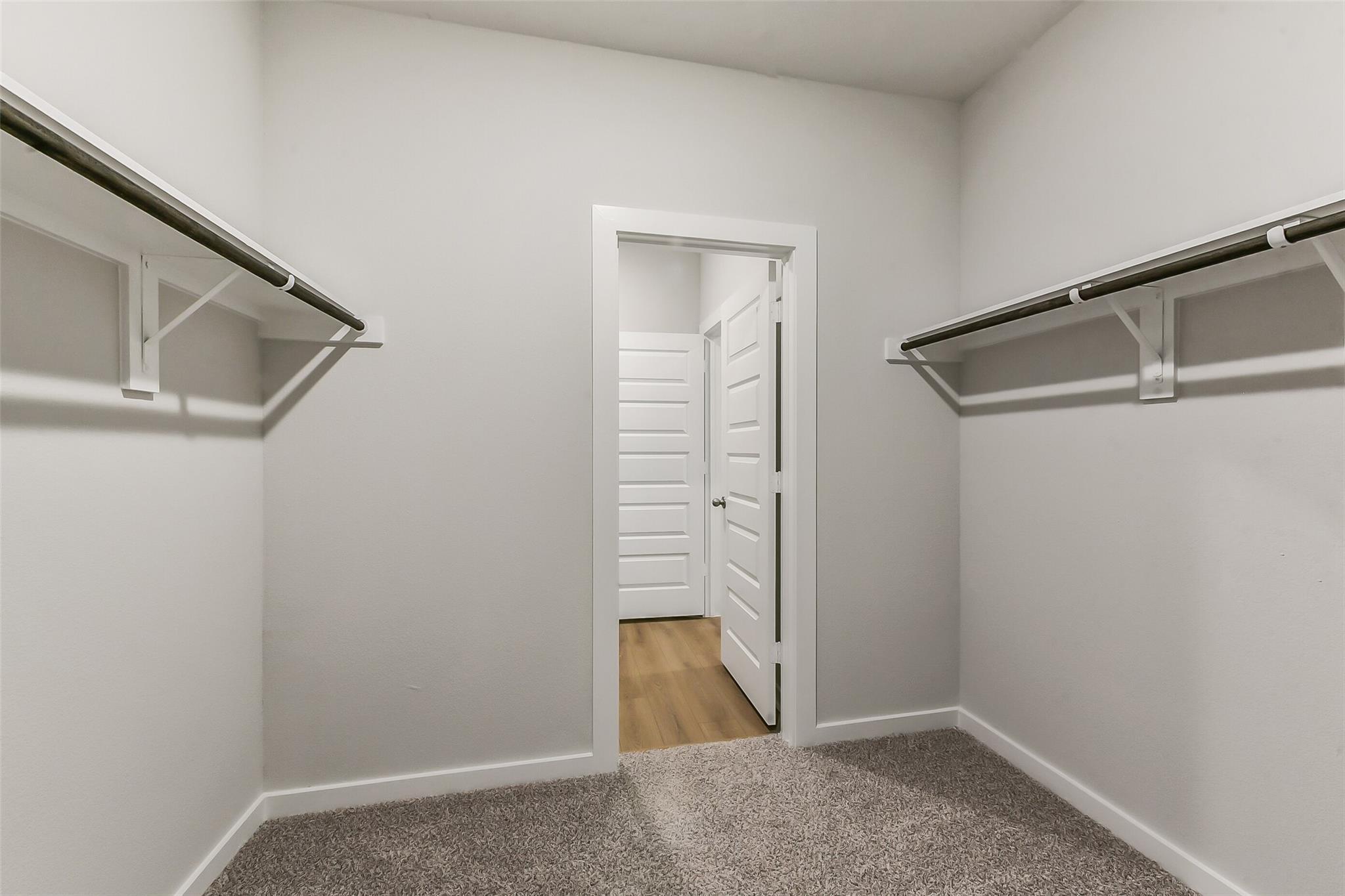 Spacious walk-in closet with white shelving and adjacent bathroom in Davidson Homes The Brazos E, Magnolia, Texas