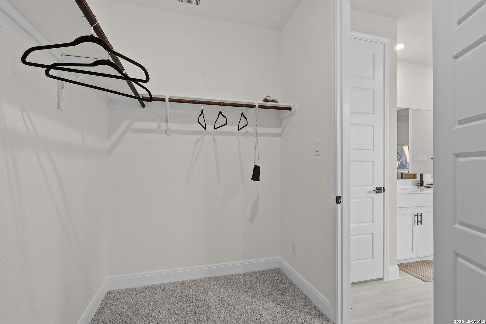 Spacious walk-in closet with wooden rods, black hangers, and shoe shelf in master suite of The Lanier G by Davidson Homes, Castroville, Texas
