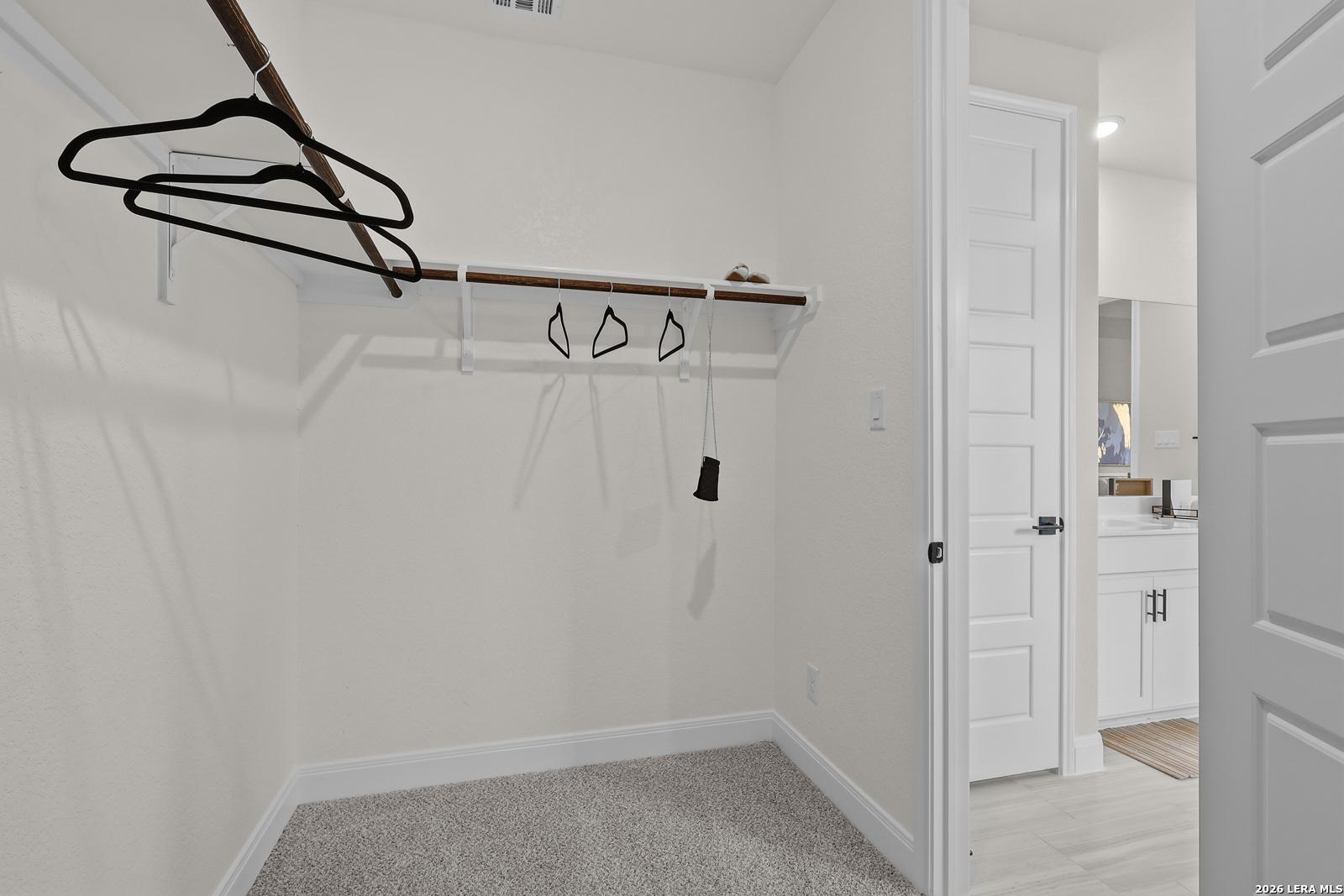 Spacious walk-in closet with wooden rods, black hangers, and shoe shelf in master suite of The Lanier G by Davidson Homes, Castroville, Texas