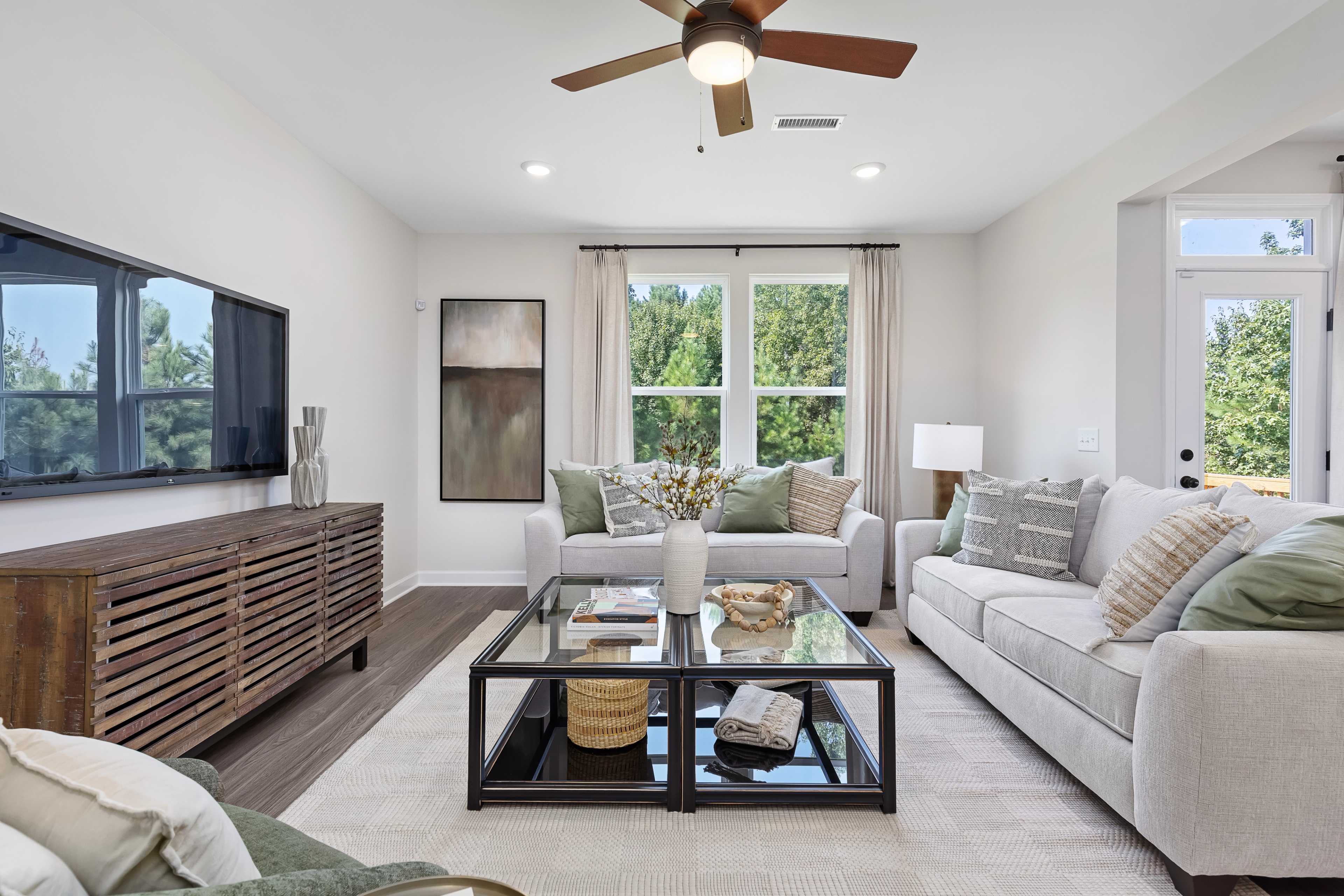 Modern living room at Woodland Crossing in Zebulon NC with beige sectional sofa, glass coffee table, ceiling fan, and large windows