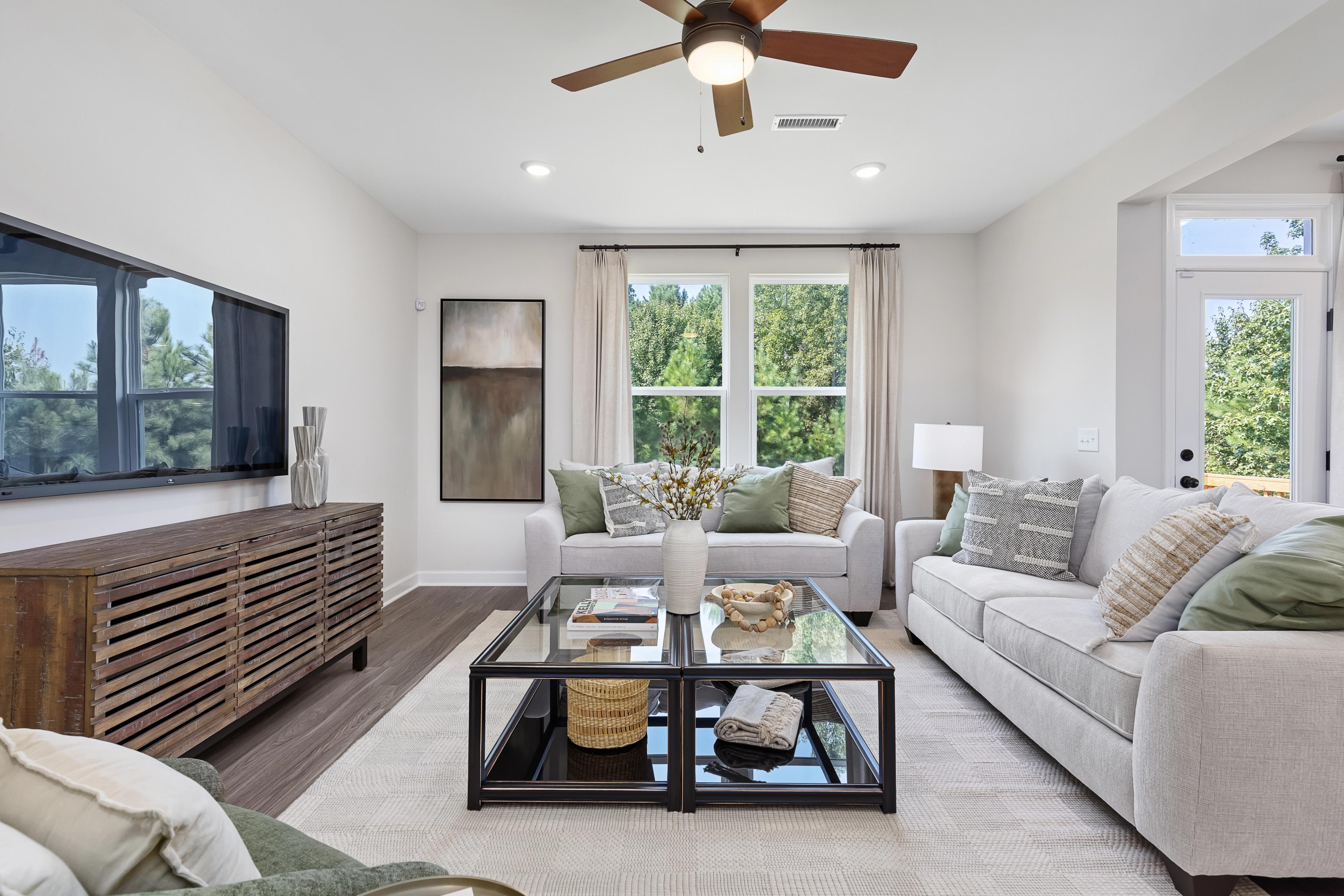 Modern living room at Woodland Crossing in Zebulon NC with beige sectional sofa, glass coffee table, ceiling fan, and large windows