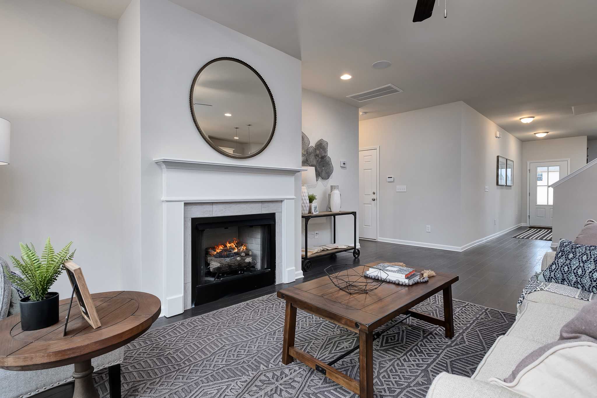 Open-concept living room at The Reserve at Overton in Hampton Cove AL featuring gas fireplace, round mirror, and modern furniture