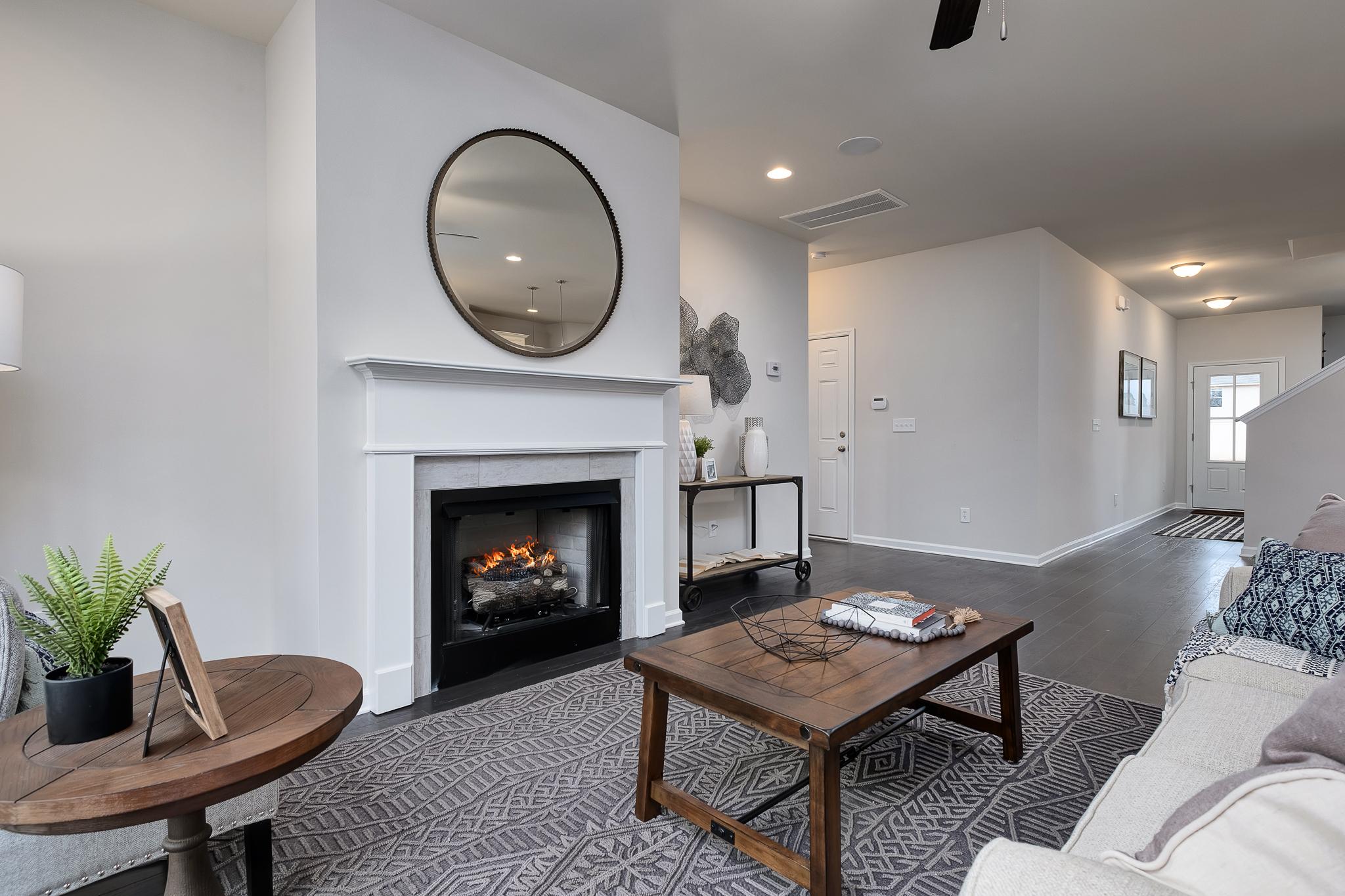 Open-concept living room at The Reserve at Overton in Hampton Cove AL featuring gas fireplace, round mirror, and modern furniture