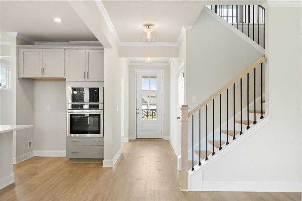 Bright foyer with white cabinets, double wall oven, oak hardwood floors, and black iron staircase in Davidson Homes The Willow D at Wehunt Meadows, Hoschton