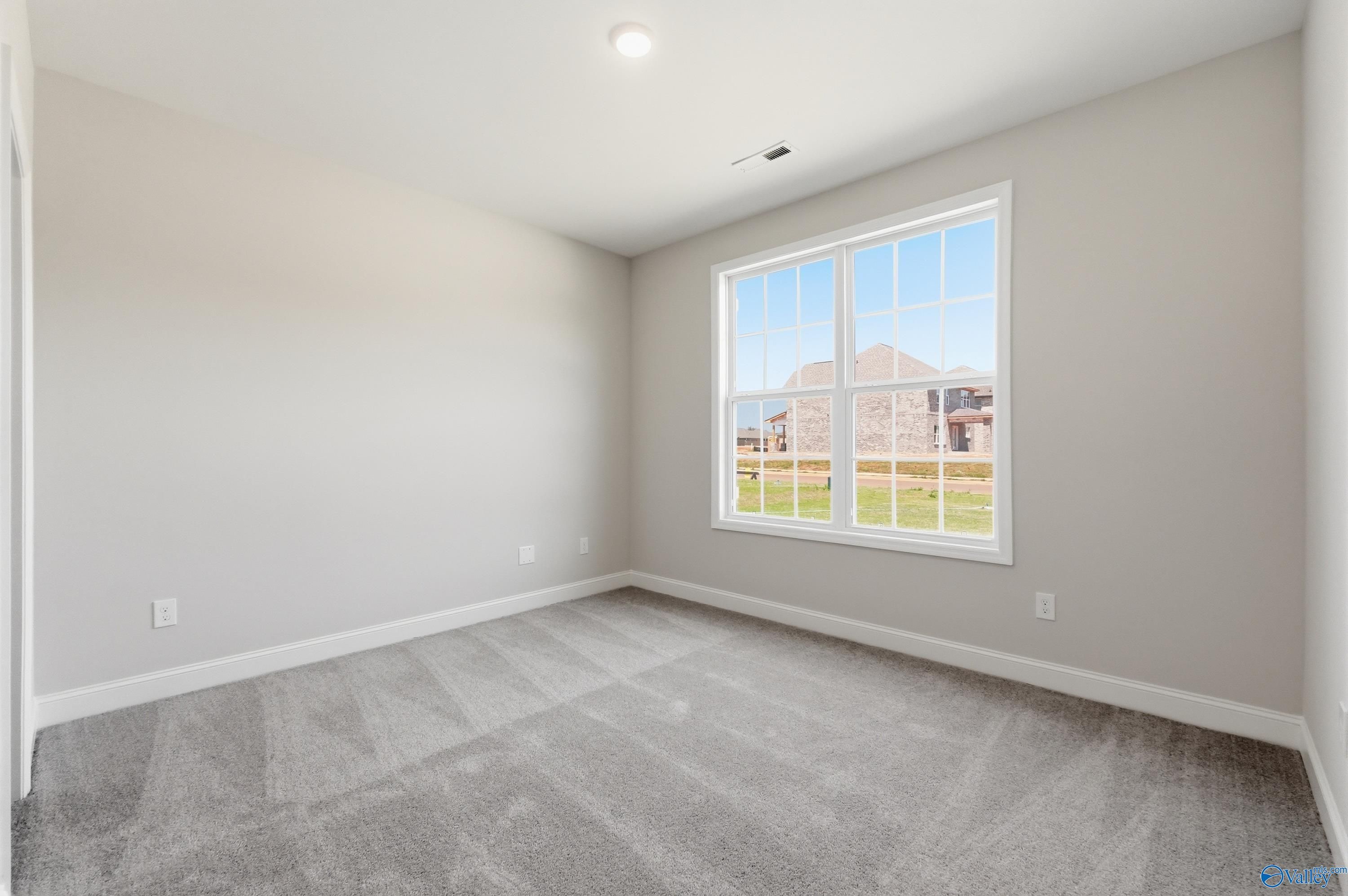 Bright empty bedroom with gray walls, carpet, and large window overlooking grassy yard in The Rockford B, Athens AL