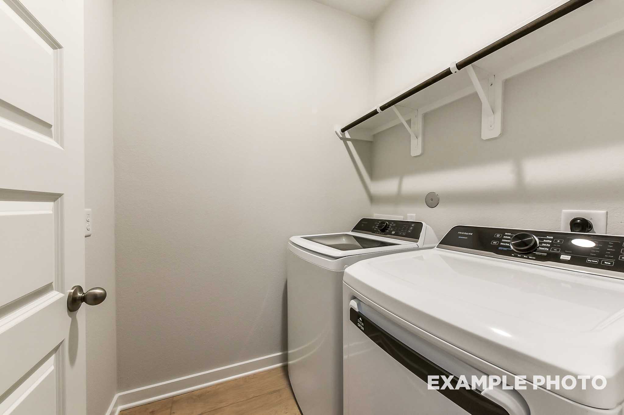 Spacious laundry room in The Laguna B with white front-load washer dryer, open shelving, neutral walls
