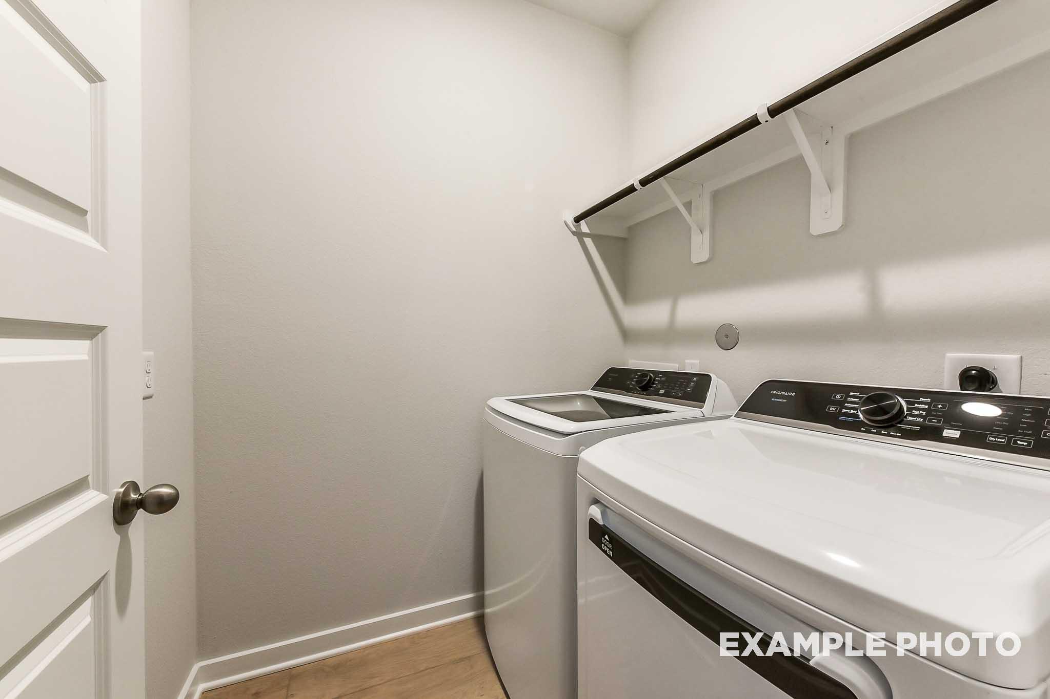 Spacious laundry room in The Laguna B with white front-load washer dryer, open shelving, neutral walls