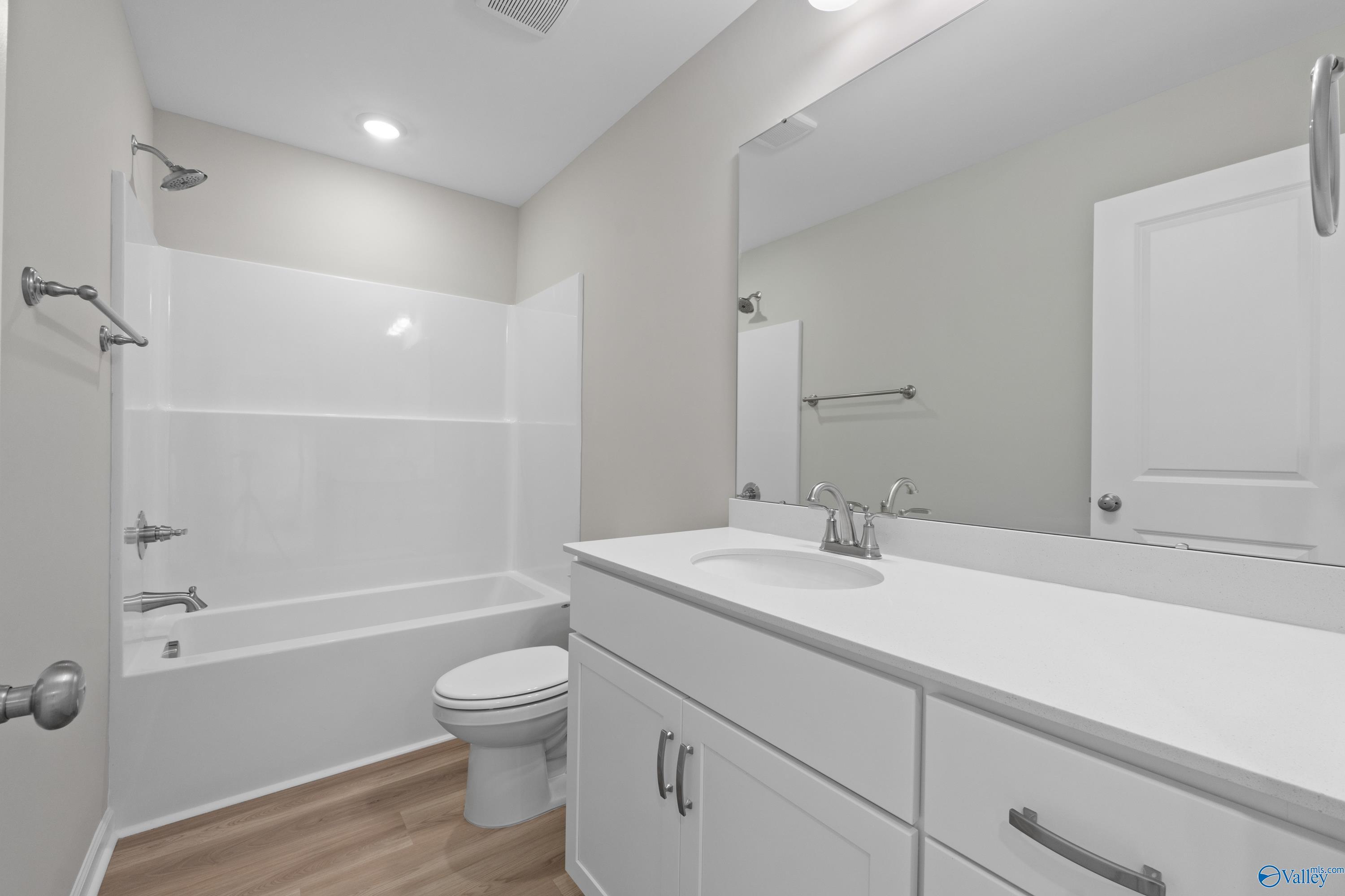 White tub-shower combo bathroom with modern vanity, mirror, and hardwood floors in Davidson Homes The Augusta, Madison, Alabama