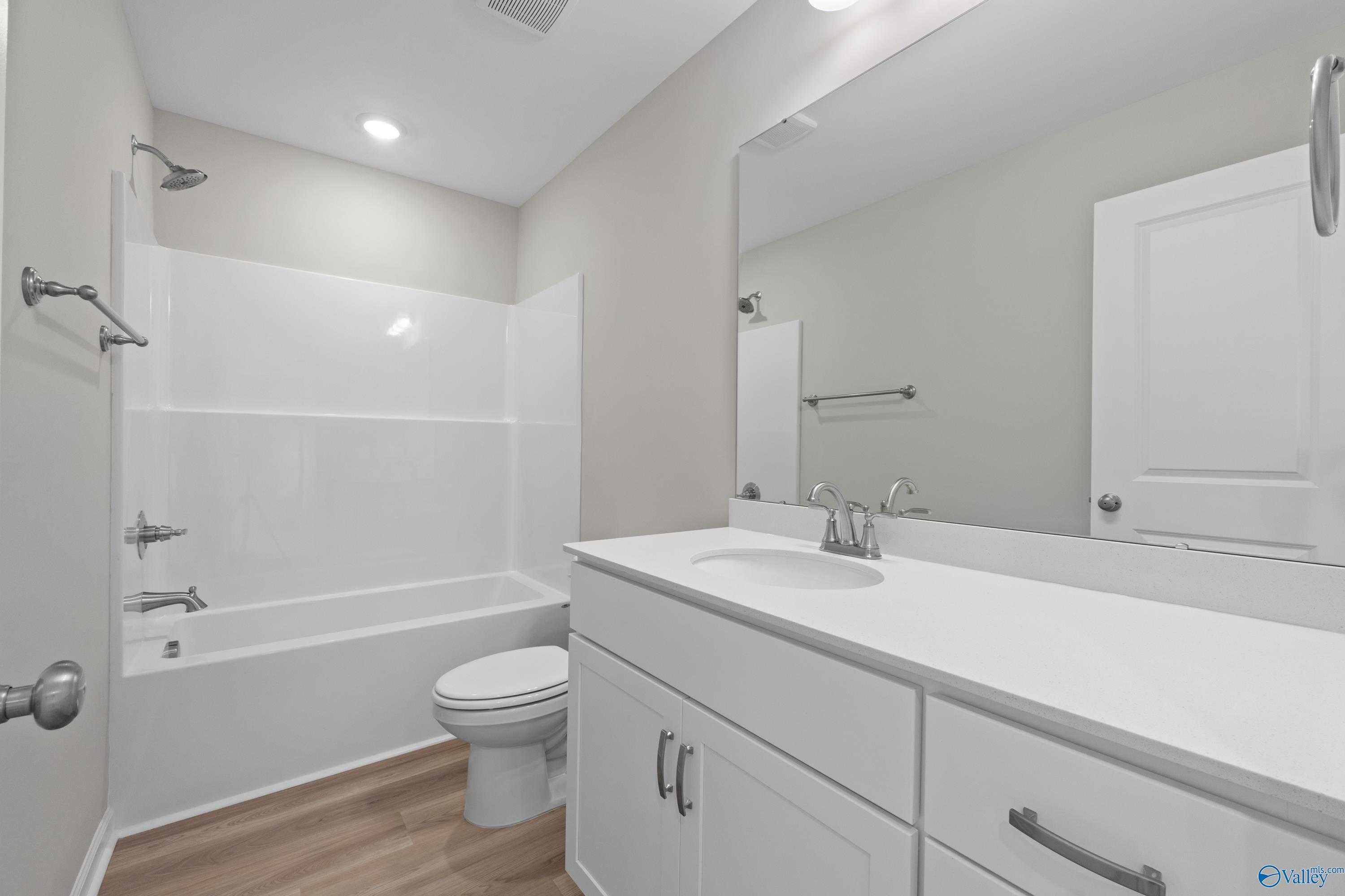 Modern bathroom with white tub-shower combo, single vanity, large mirror, and neutral walls in Evermore Homes The Augusta, Madison, Alabama