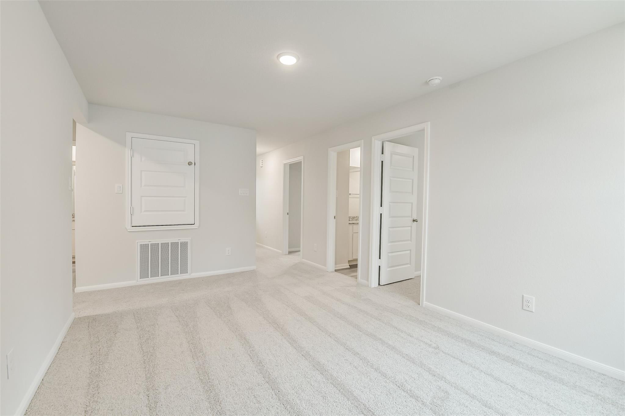 Bright carpeted hallway with white doors, open entries, and recessed lighting in Davidson Homes The Brazos F, Conroe, Texas