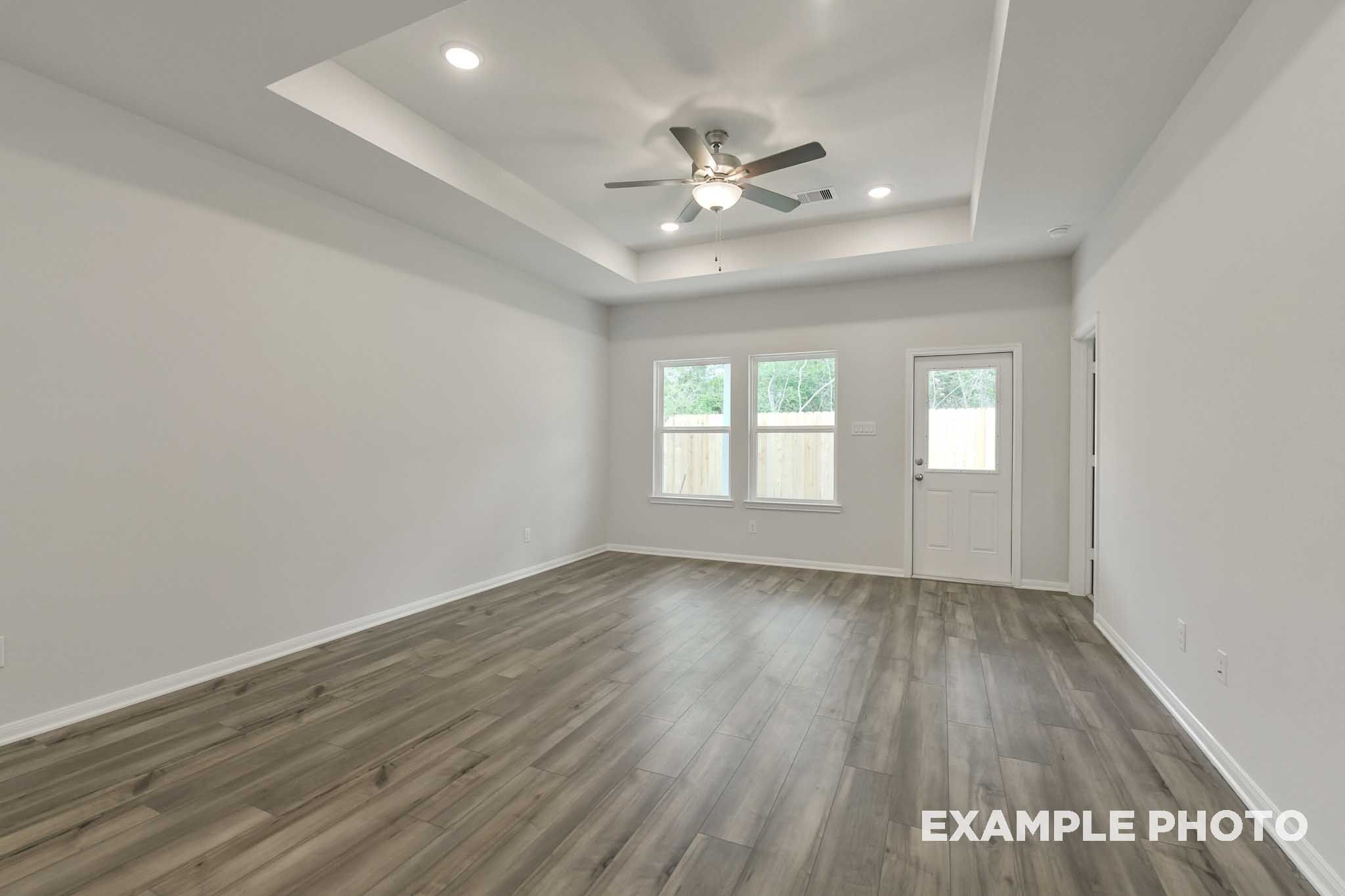 Spacious living area in The Frio floor plan featuring a tray ceiling, ceiling fan, and durable wood-look flooring.