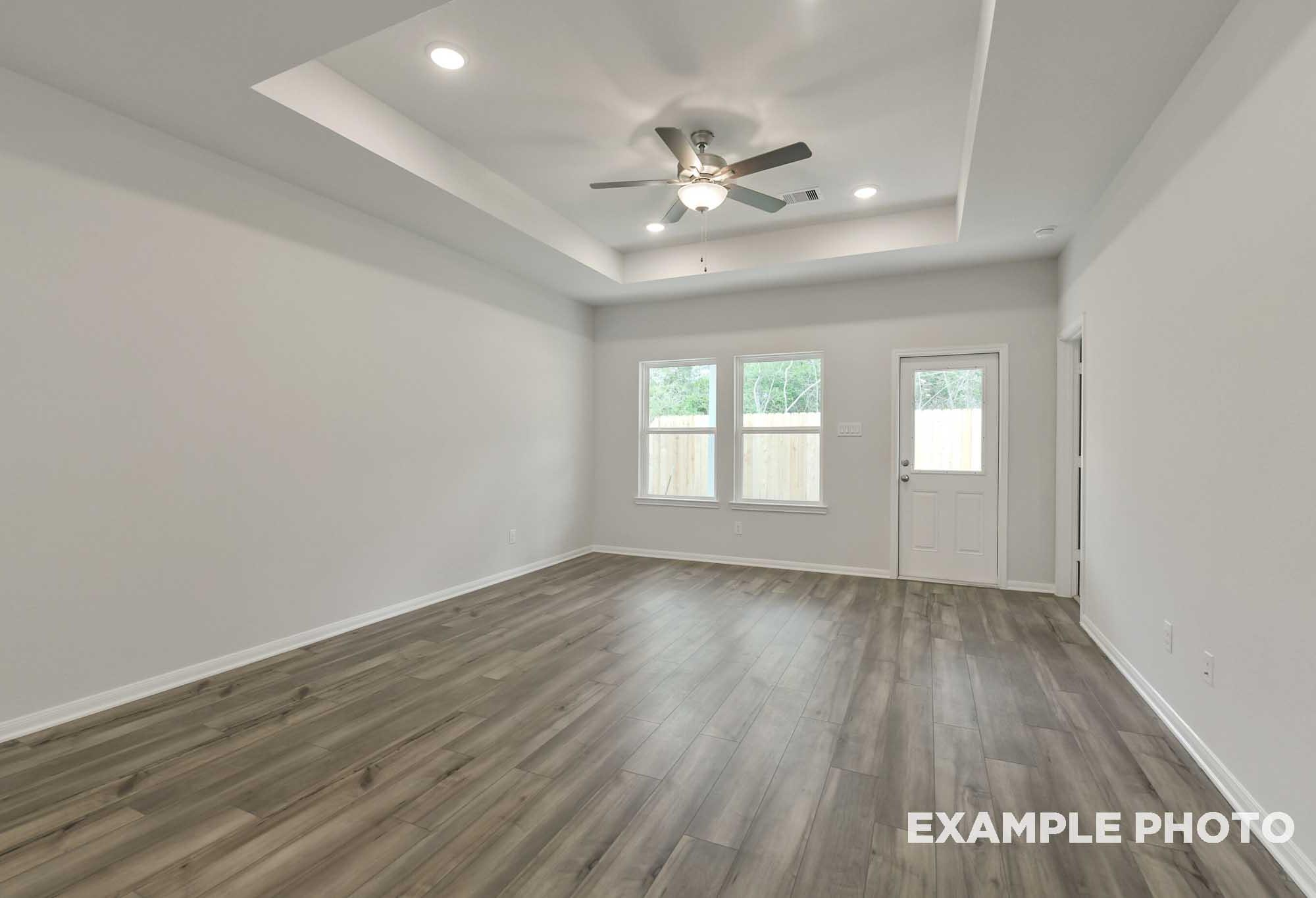 Spacious living area in The Frio floor plan featuring a tray ceiling, ceiling fan, and durable wood-look flooring.