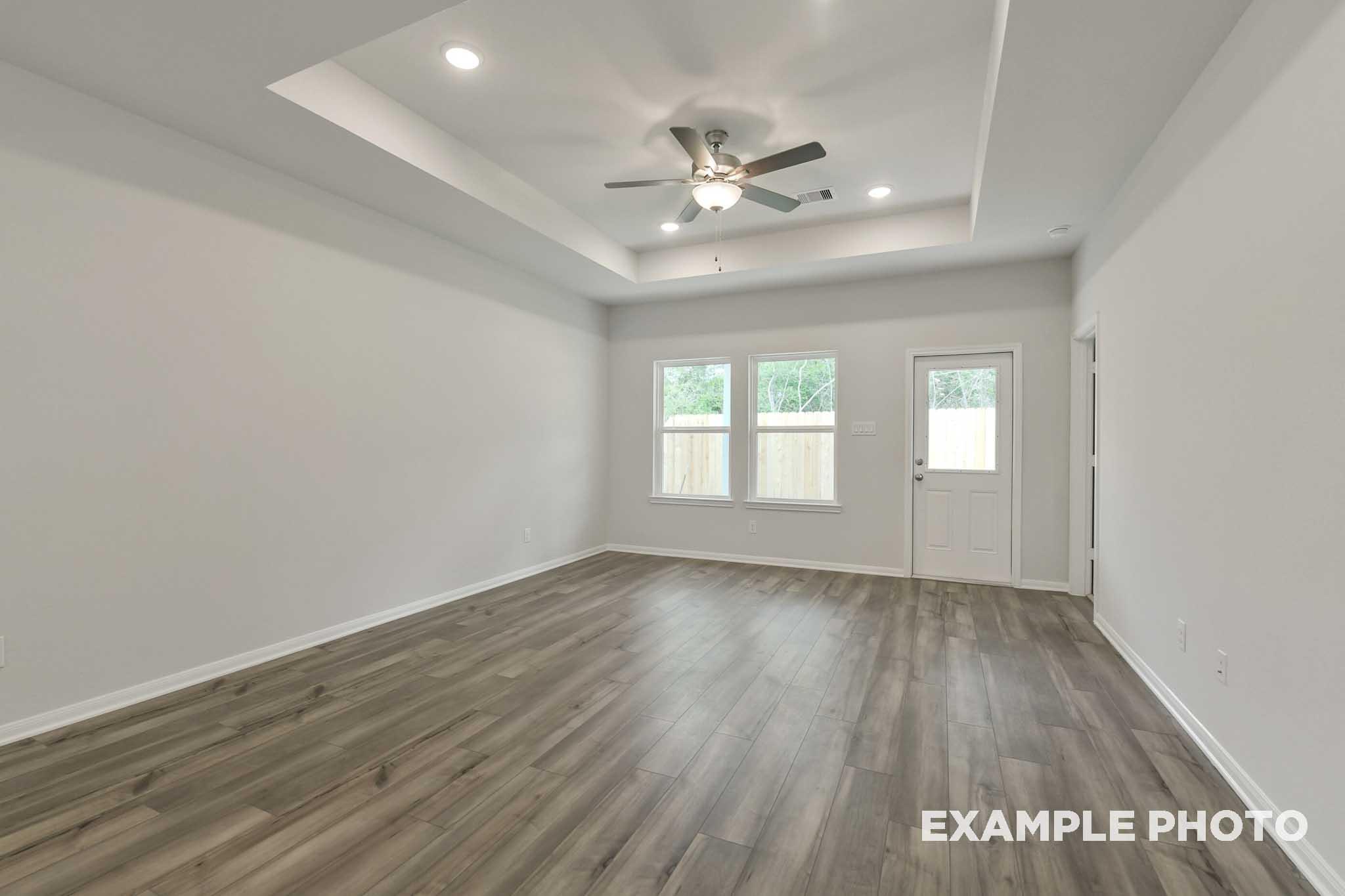 Spacious living area in The Frio floor plan featuring a tray ceiling, ceiling fan, and durable wood-look flooring.