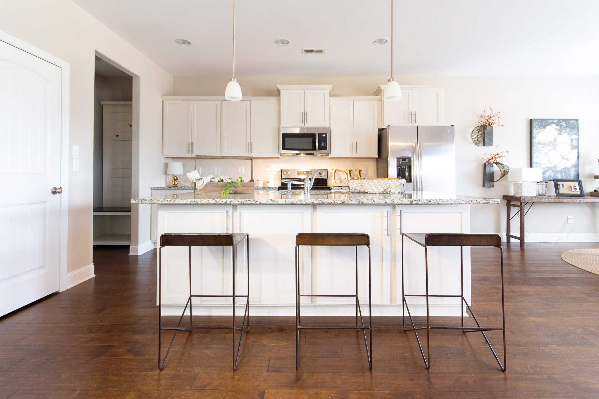 Spacious white kitchen in Summer Pointe Madison AL with center island, bar stools, stainless appliances, hardwood floors