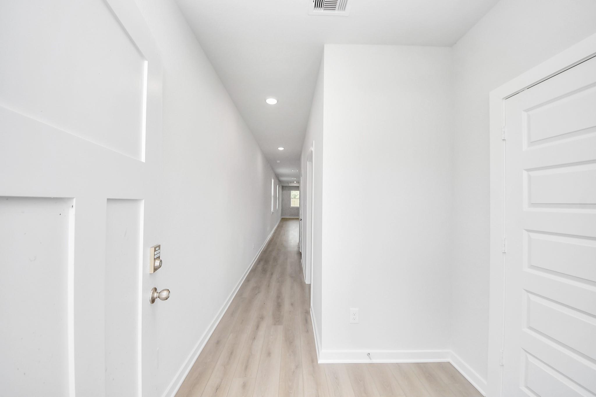 Bright, modern hallway with wood-style flooring in The Frio F floor plan at Liberty Estates in Cleveland, Texas.