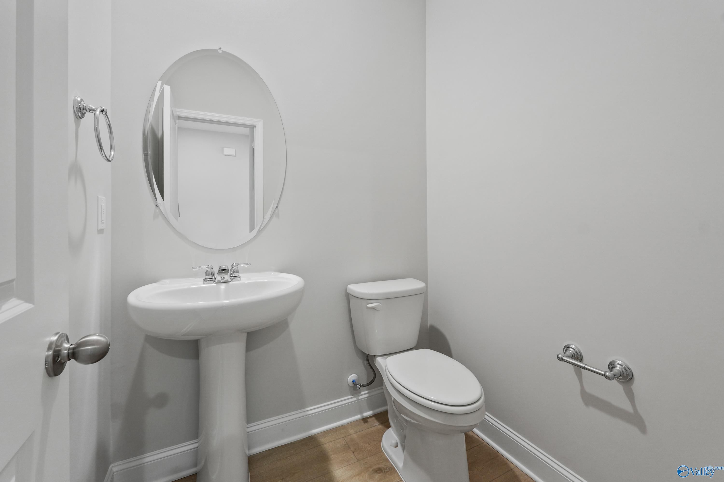 Modern powder room with white pedestal sink, round mirror, and toilet in Davidson Homes The Camden B, Huntsville, AL