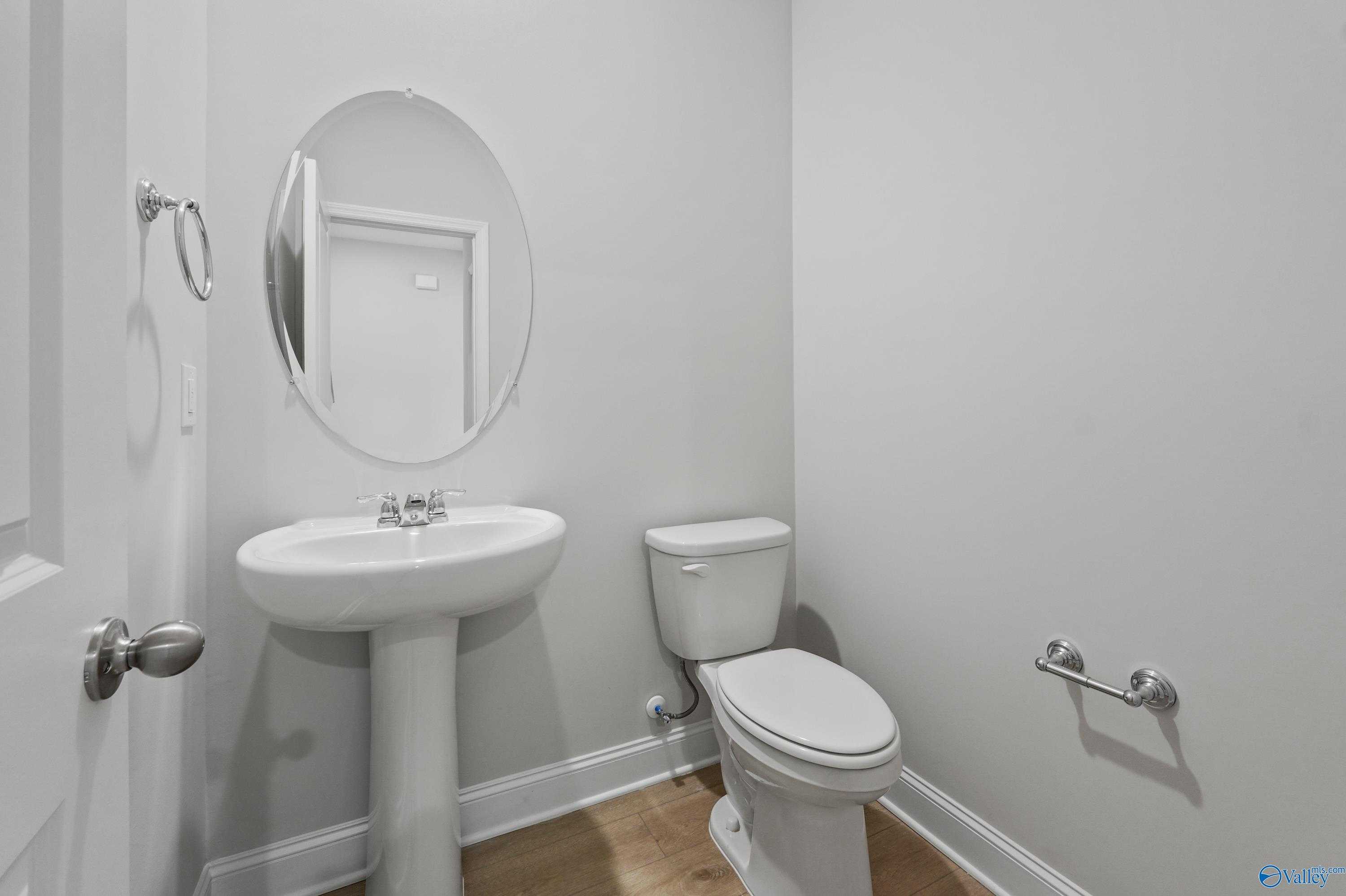 Modern powder room with white pedestal sink, round mirror, and toilet in Davidson Homes The Camden B, Huntsville, AL