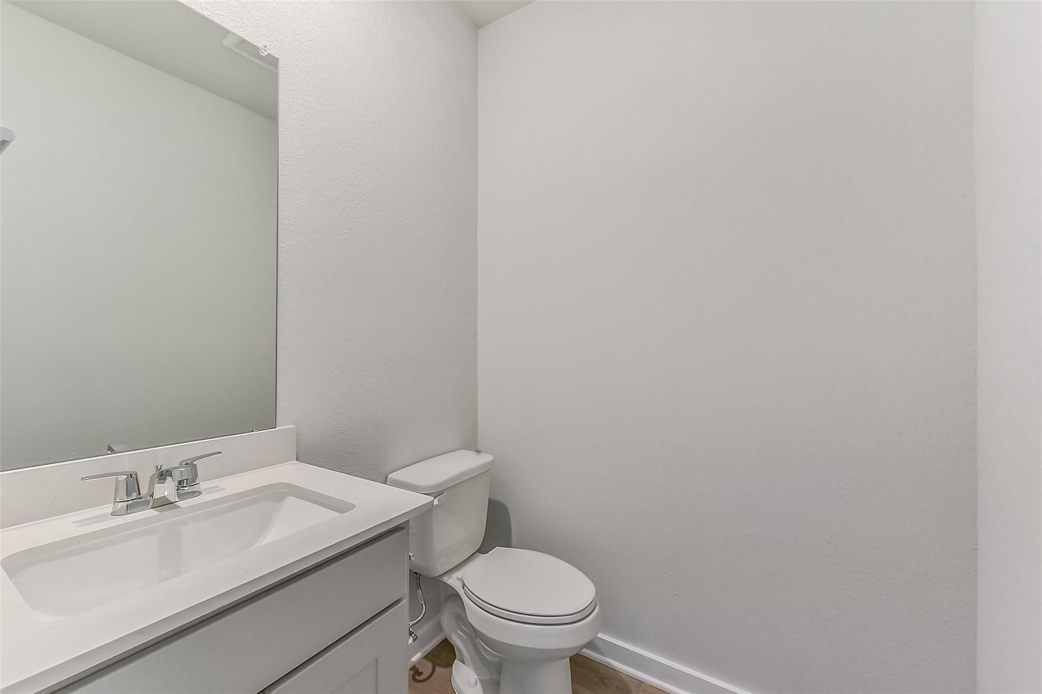 Modern half bath with white vanity sink, chrome faucet, mirror, and toilet in Davidson Homes The Tierra C, Dayton, Texas