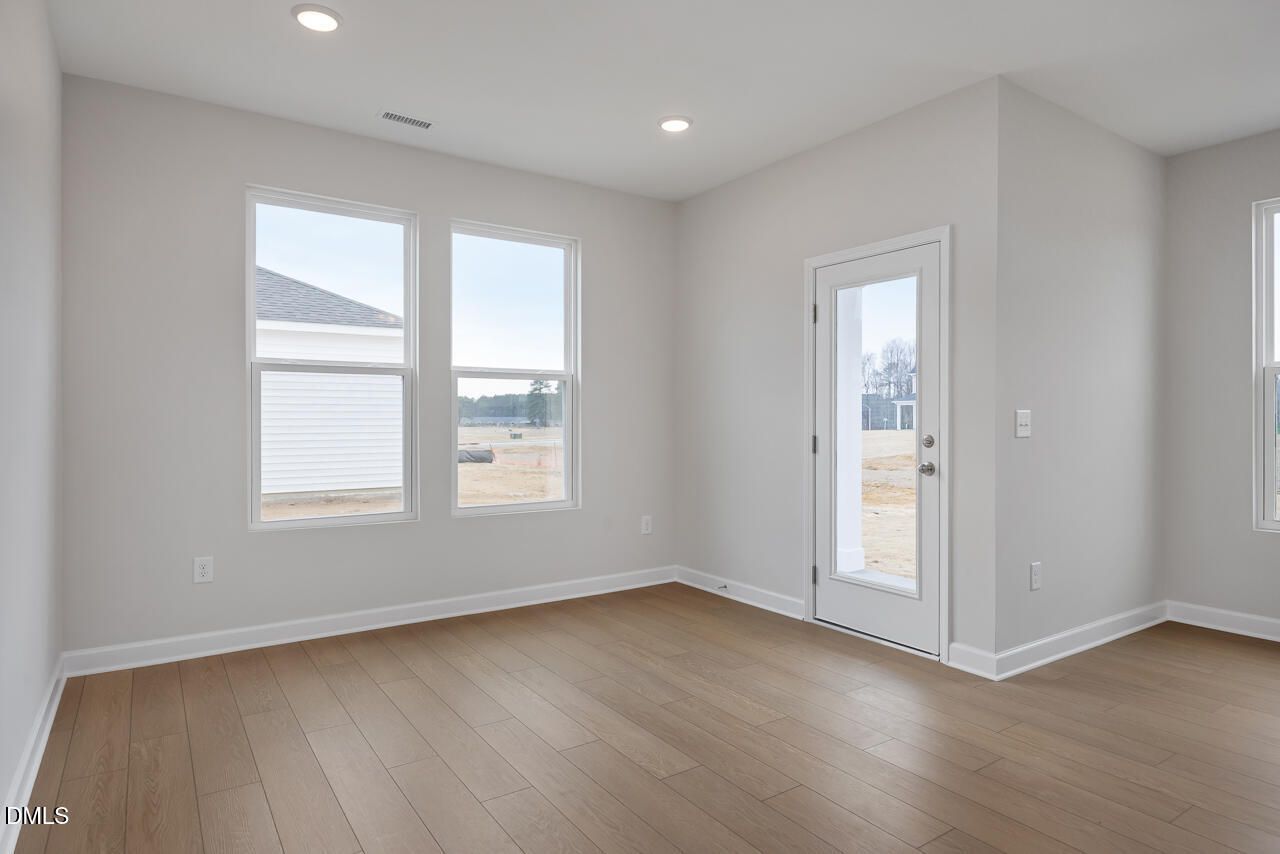 Spacious empty living room with light gray walls, hardwood floors, and large windows in The Daphne C 3-bedroom home, Lillington, NC