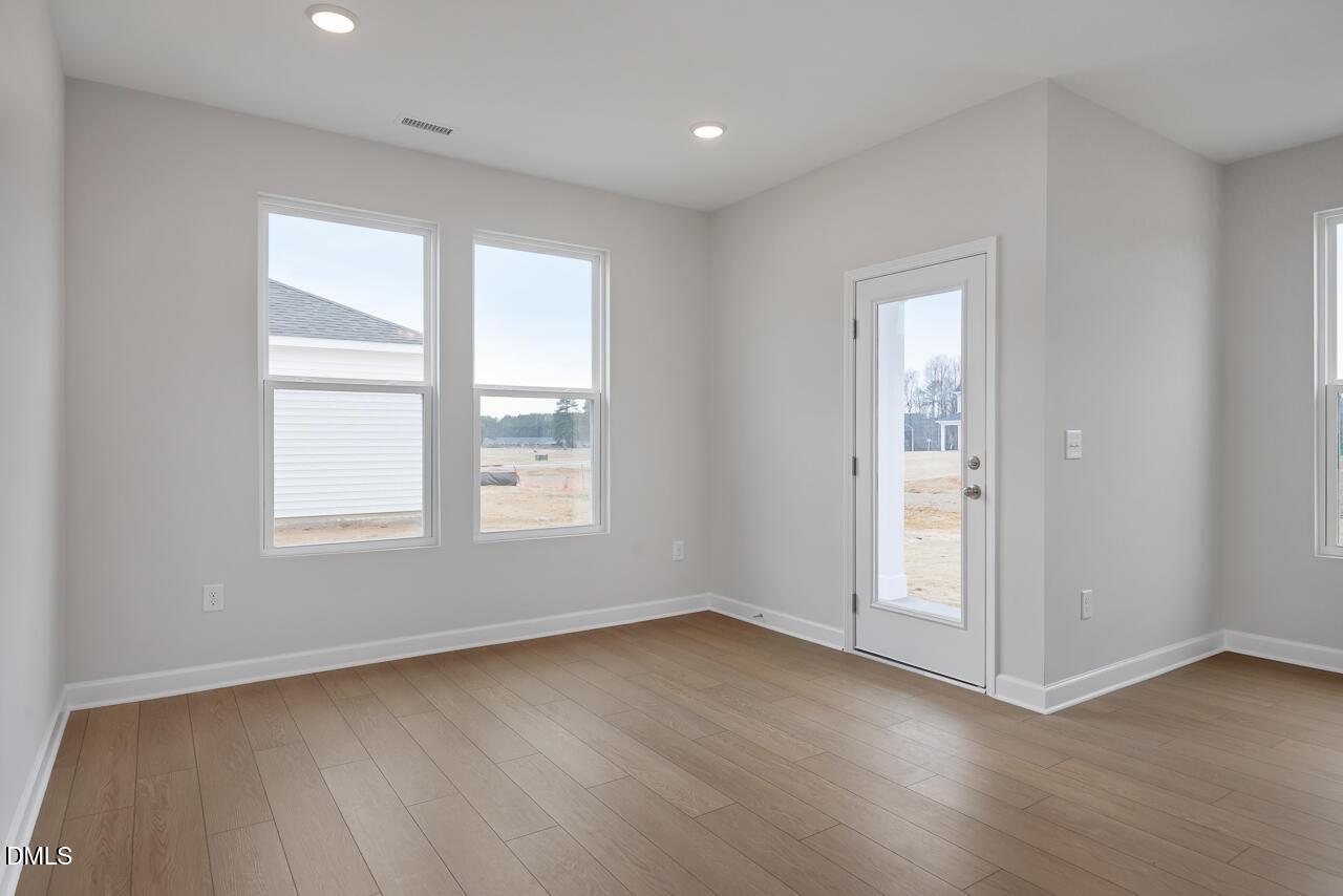 Spacious empty living room with light gray walls, hardwood floors, and large windows in The Daphne C 3-bedroom home, Lillington, NC